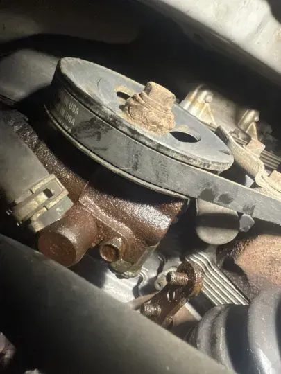 Rust-covered water pump in an engine compartment with pulley and belt visible.