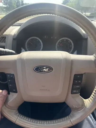 Beige Ford steering wheel, dashboard visible. Sun glare.