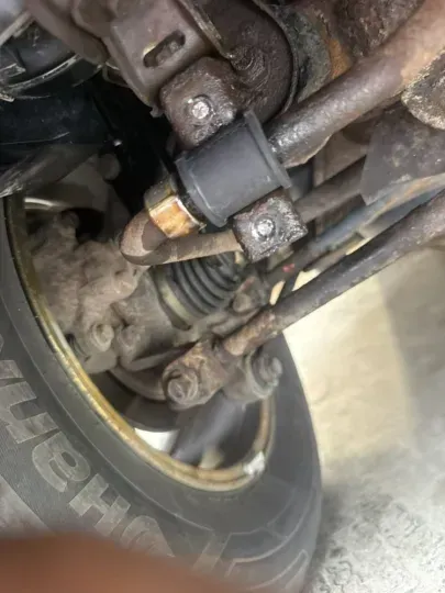 Undercarriage view of a vehicle's suspension components, including a sway bar and bushings, near a wheel.