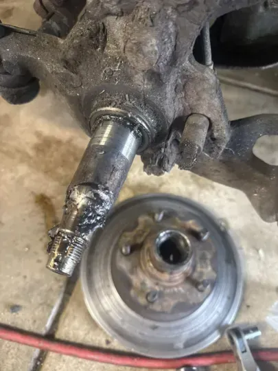 Worn vehicle suspension components including hub, rotor, and spindle with welding damage.