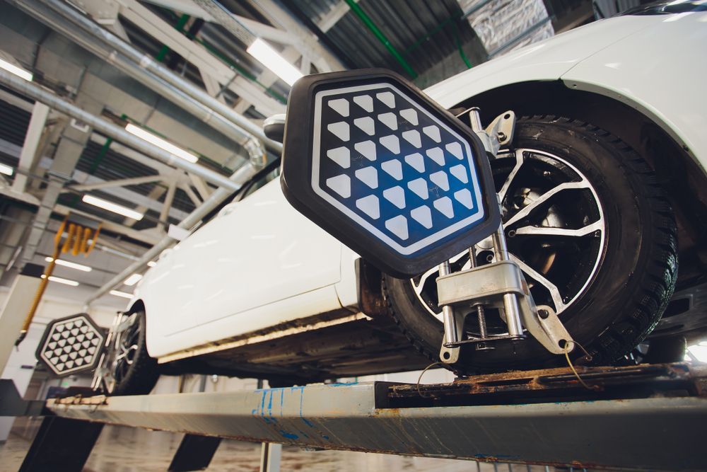 White car on a lift, undergoing wheel alignment; sensors on wheels with blue and white targets.