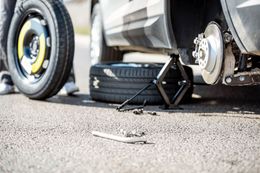 Car tire change: spare tire, car jack, and lug wrench on asphalt.