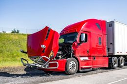 Red semi-truck with open hood on the side of a road, bright sunny day.