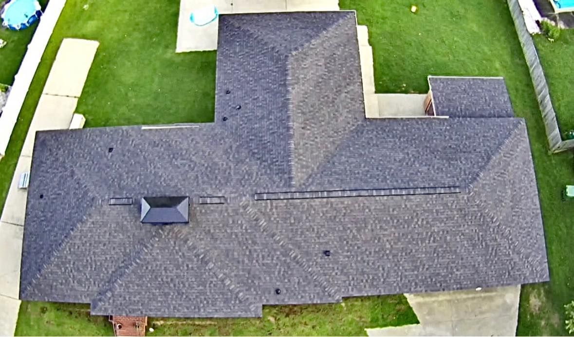 Overhead view of a house with a dark gray shingled roof, set on green grass.