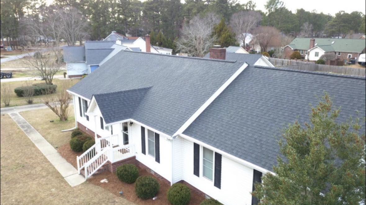 White house with dark gray roof, black shutters, and front porch; trees in the background.