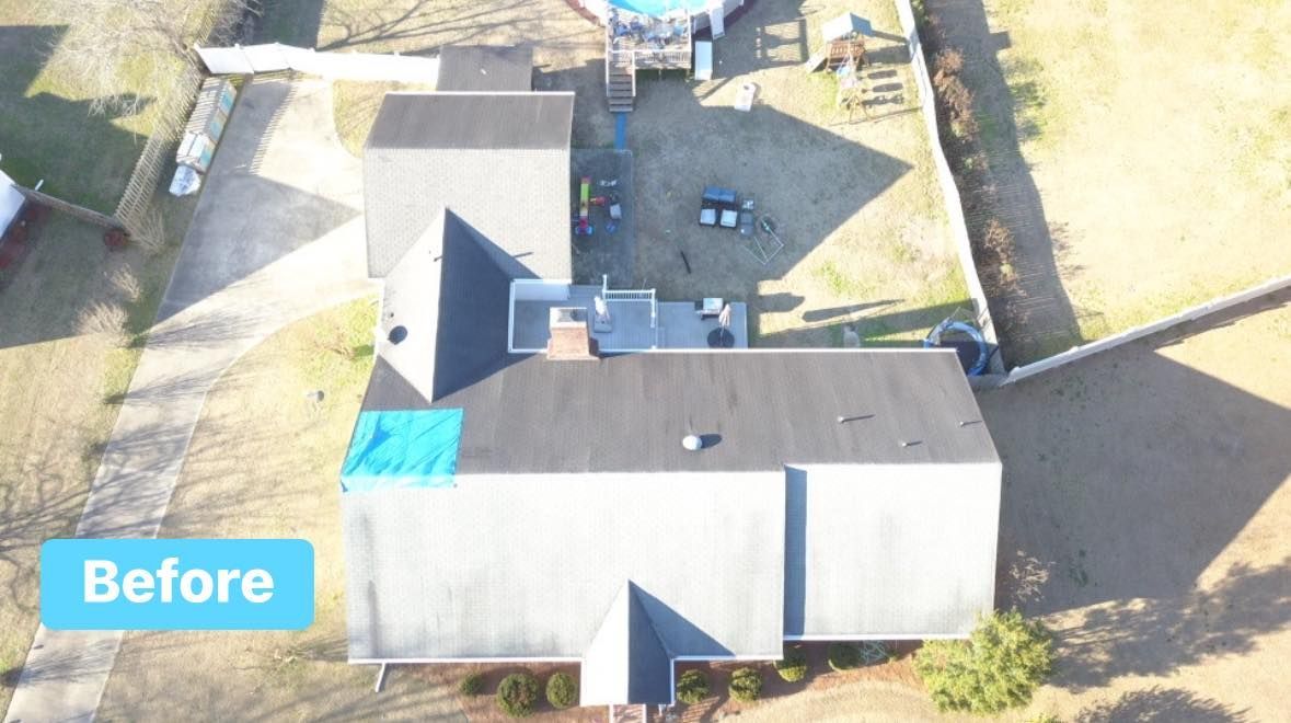 Overhead view of a house with a dark roof and a tarp patch, before repair, surrounded by yard.