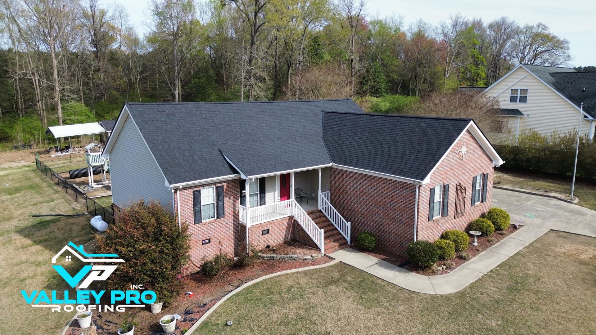A brick and siding house with a dark roof in a yard. Trees in the background, a logo in the bottom left.
