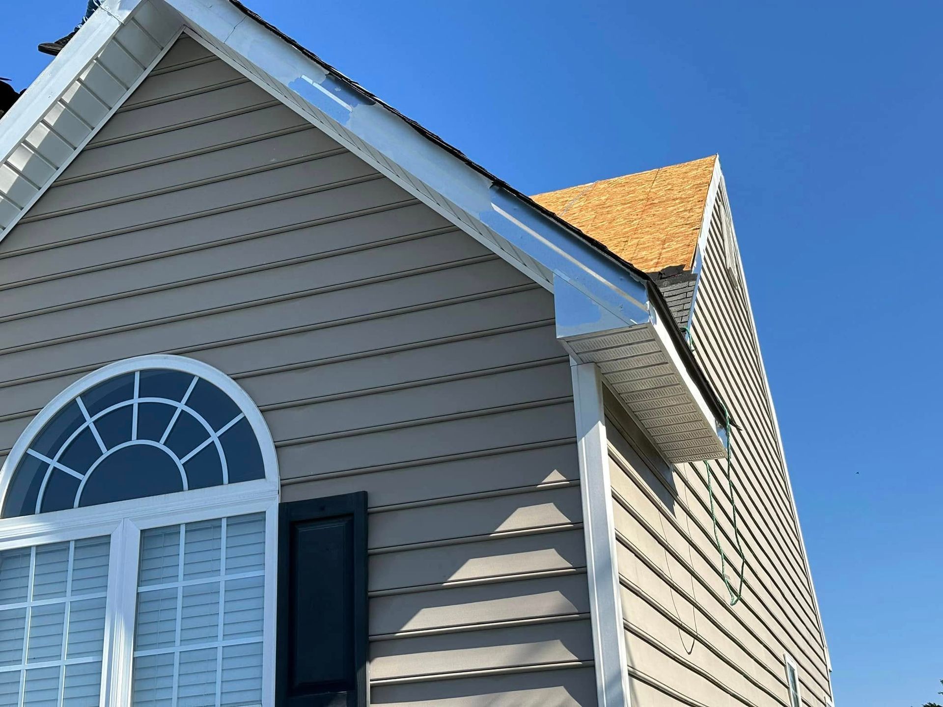 Tan house with a white trim and a section of roof partially under construction; blue sky.