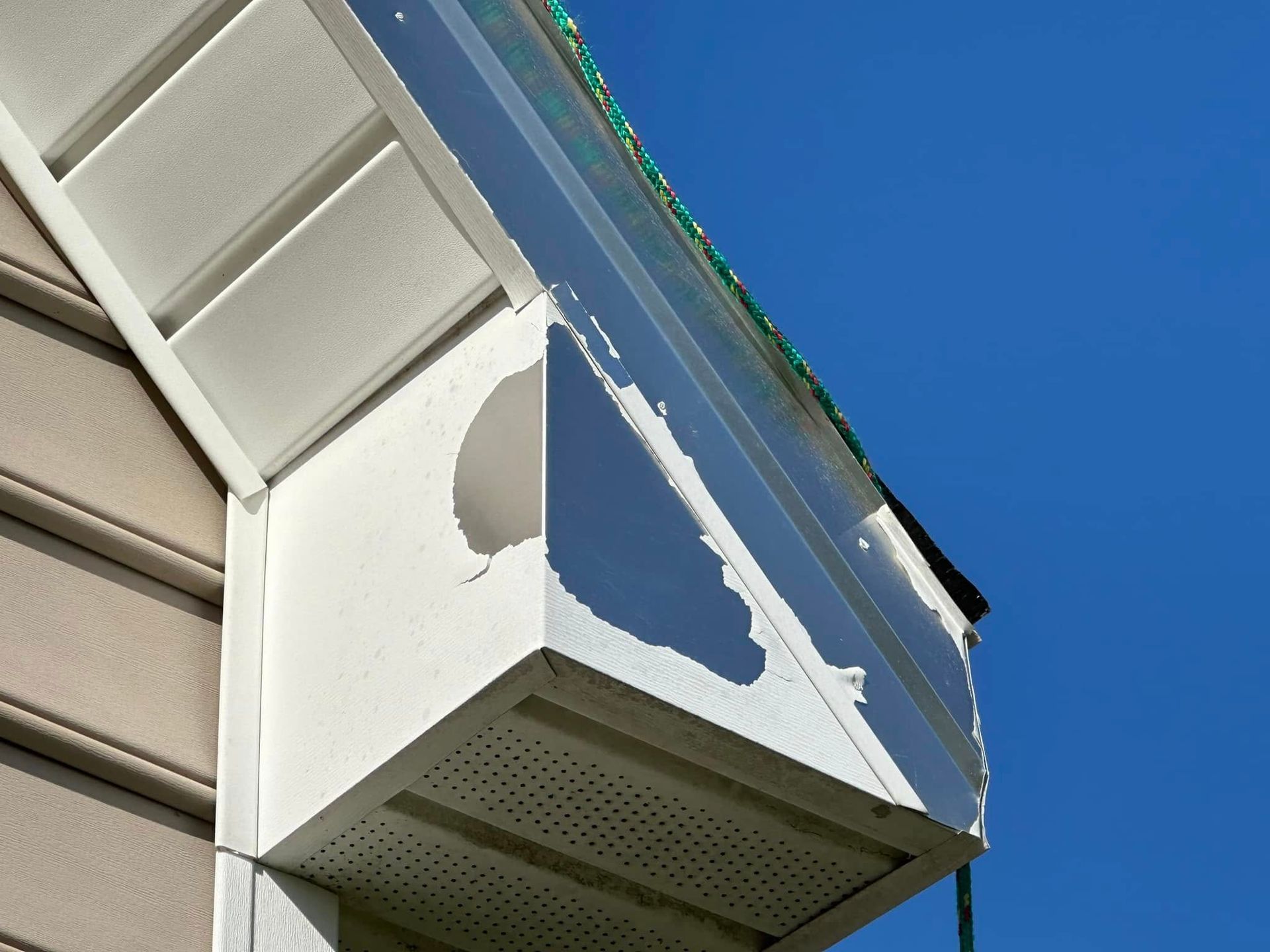 Damaged white soffit and gutter on a house, with blue sky background.