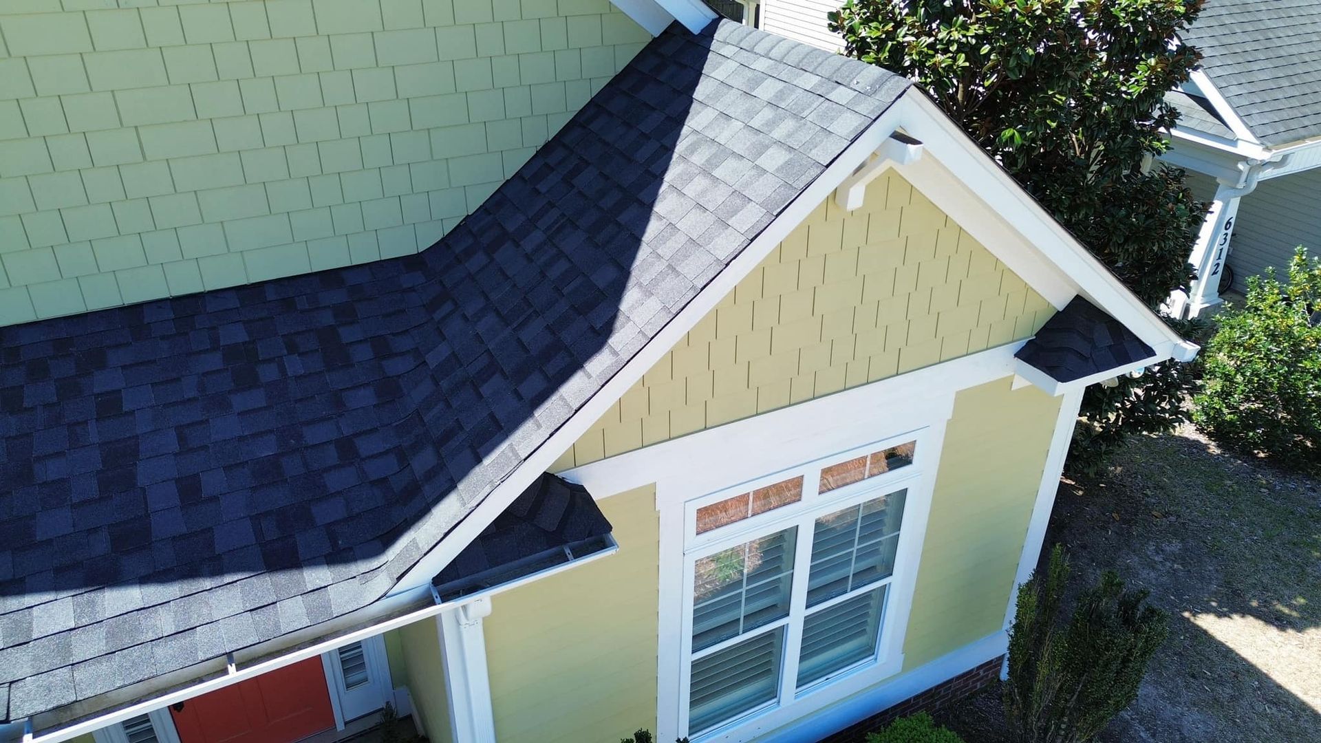 Overhead view of a house with dark roof shingles, yellow siding, white trim, and a window.