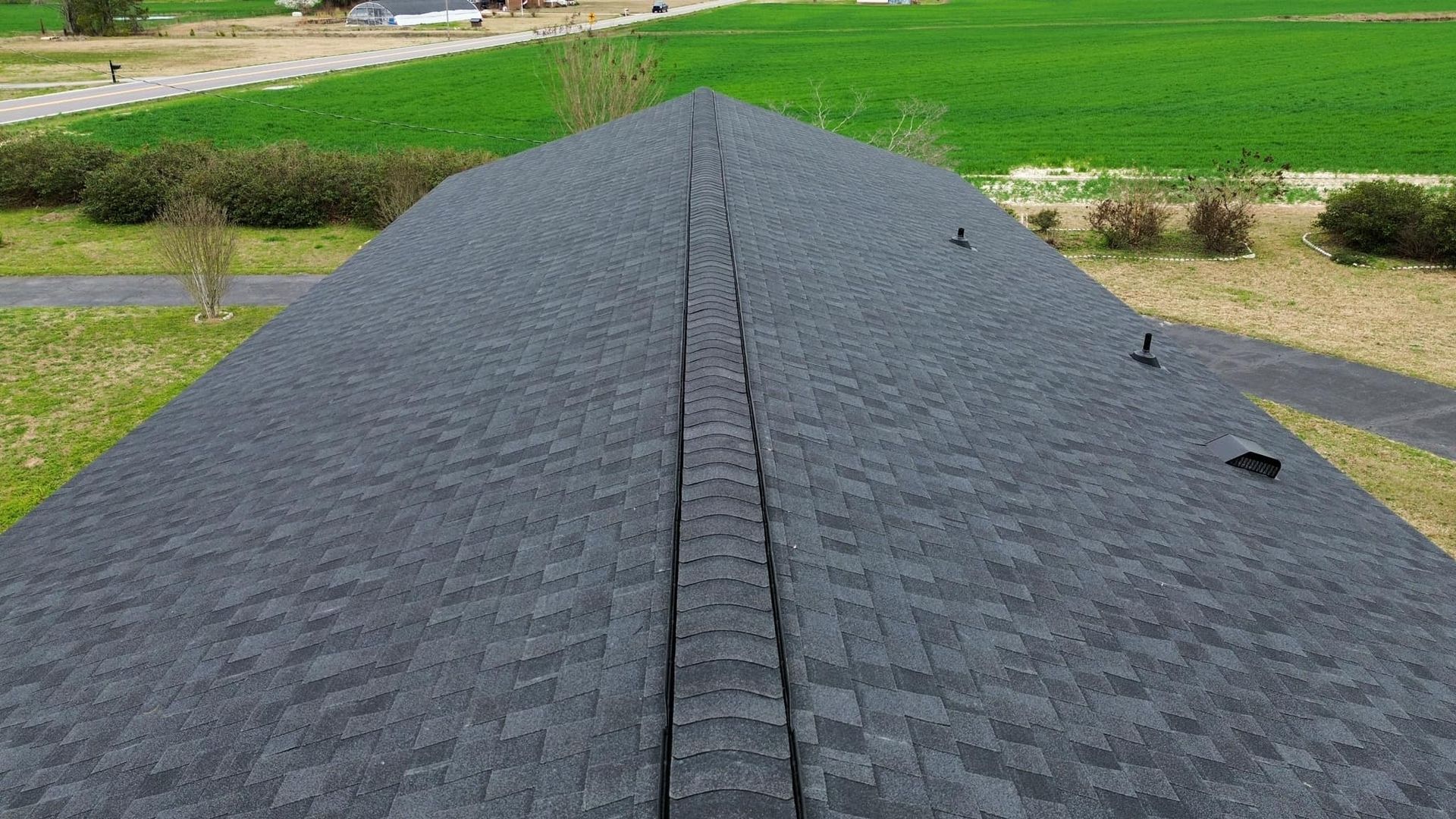Gray asphalt shingle roof on a house, with a long, grassy yard in the background.