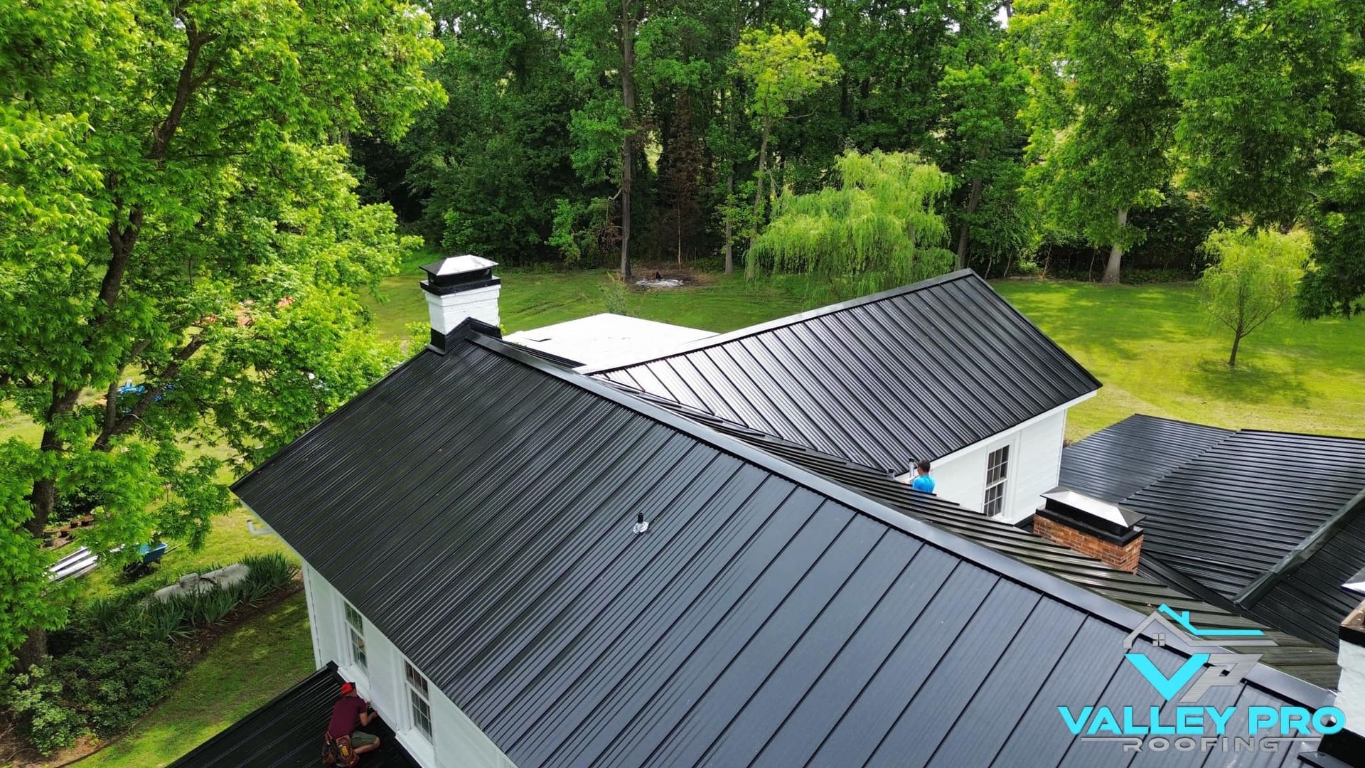 Black metal roof on white house, surrounded by trees.