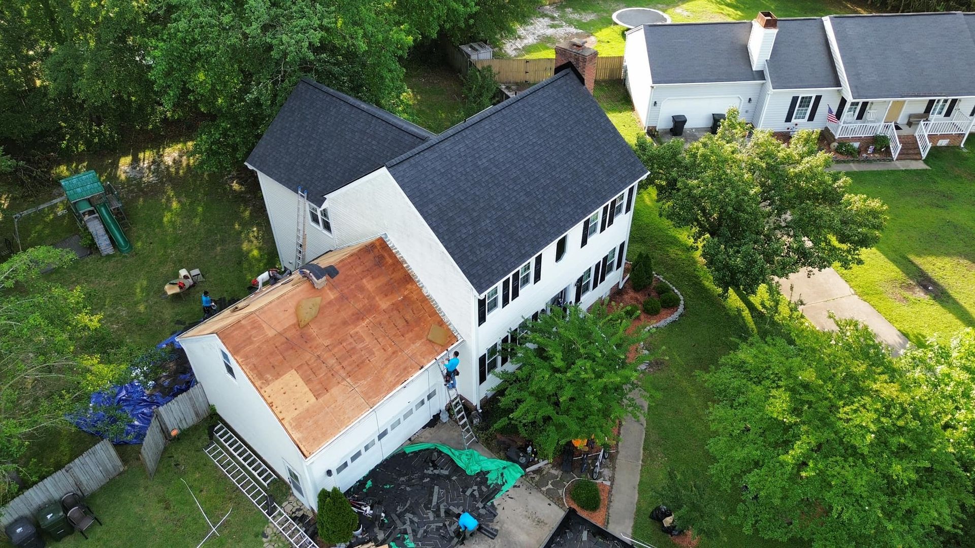 Aerial view of a white house with a partially replaced black roof. Construction debris is visible on the ground.