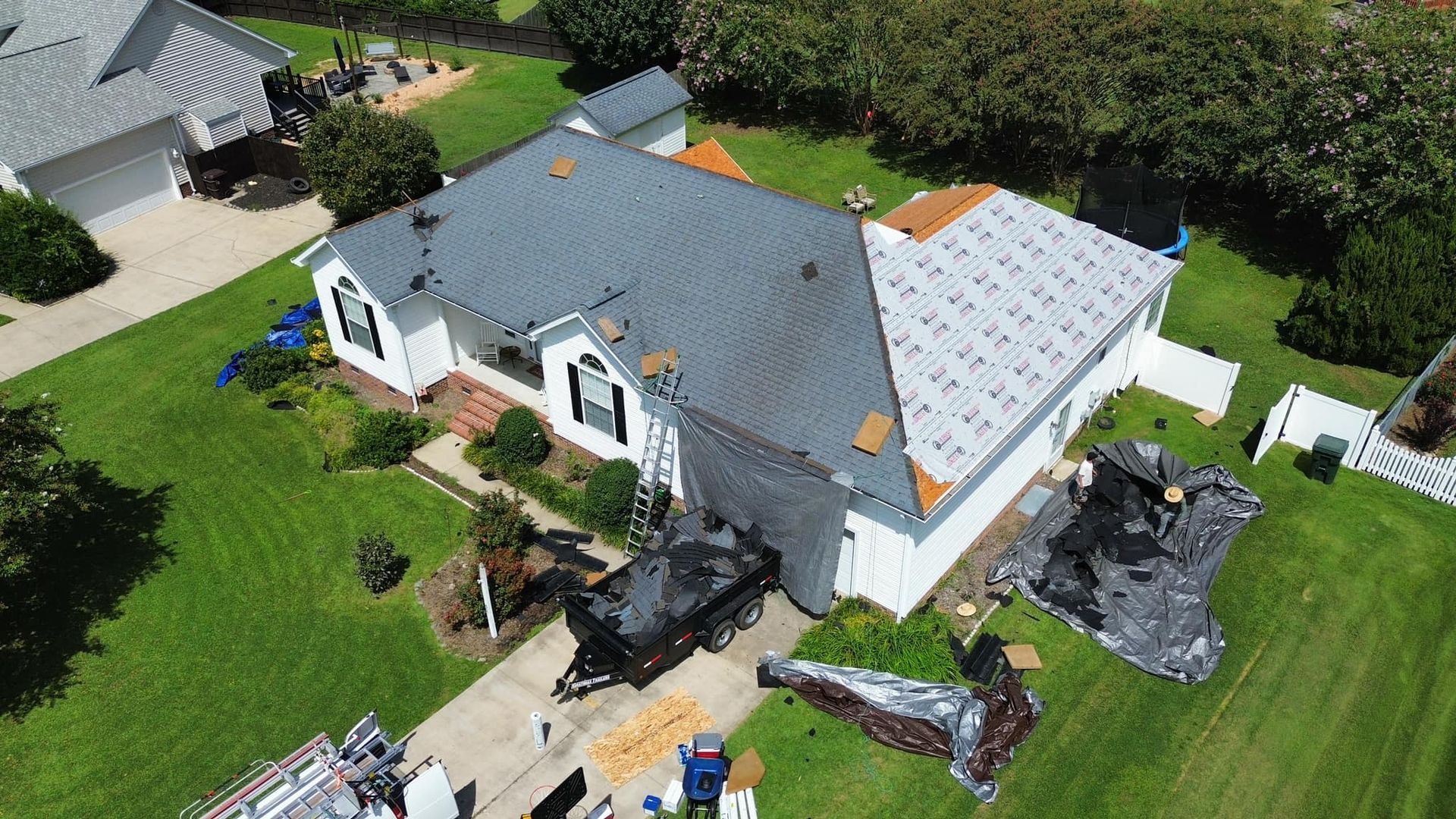 Aerial view of a house undergoing roof replacement; one side is new grey shingles, the other old and exposed.