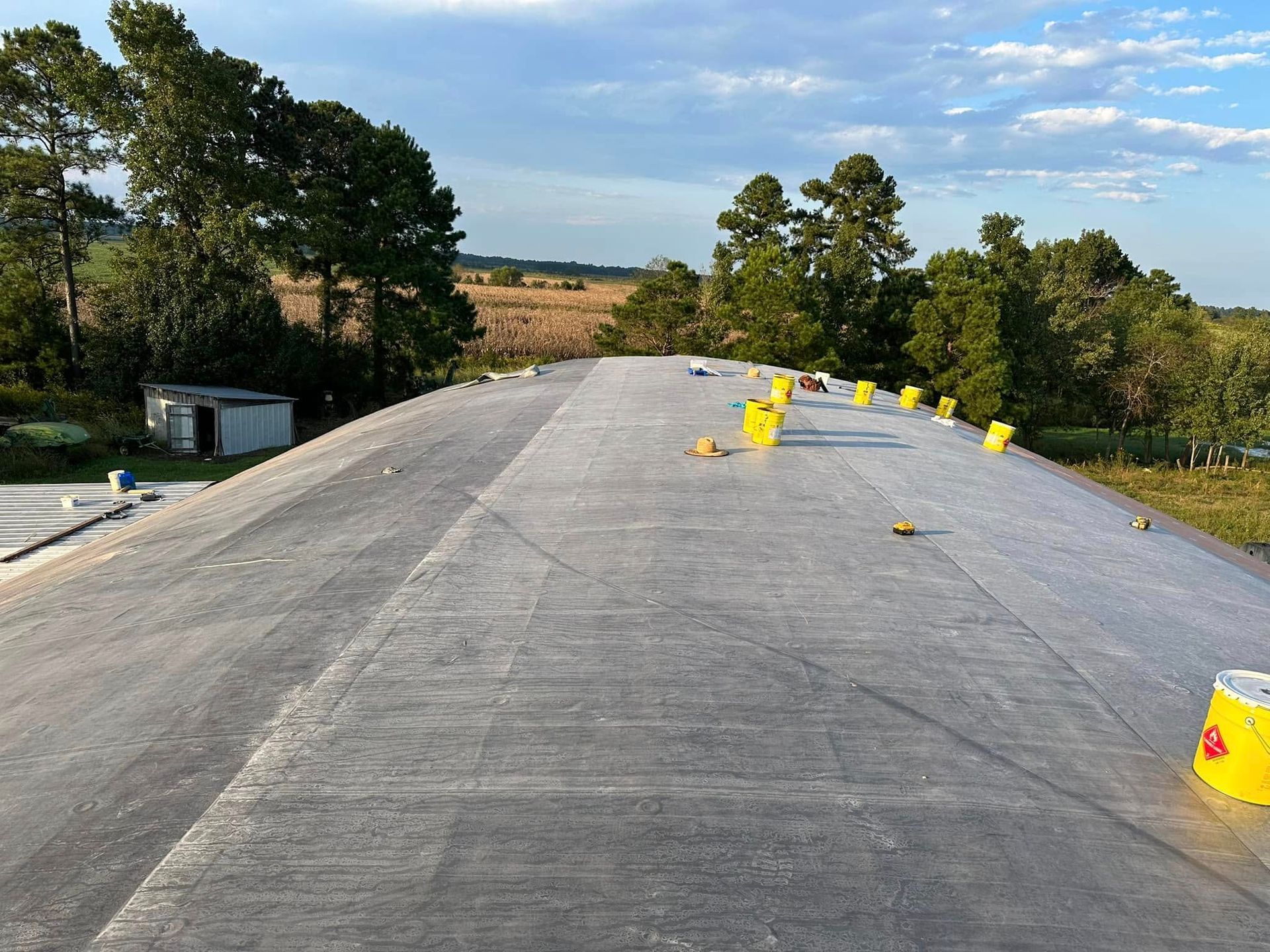A low-slope roof of a building with a landscape in the background. Yellow buckets are spaced on the roof.