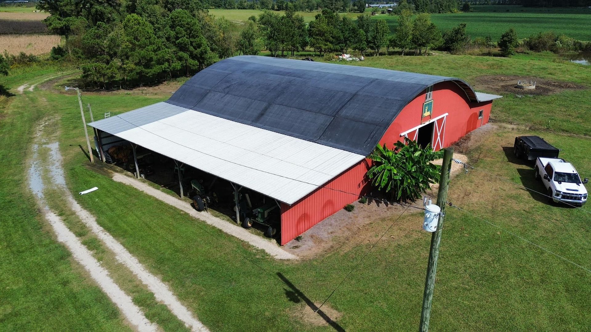 Red barn with curved black roof, white trim. Grassy yard with white truck and dirt path.
