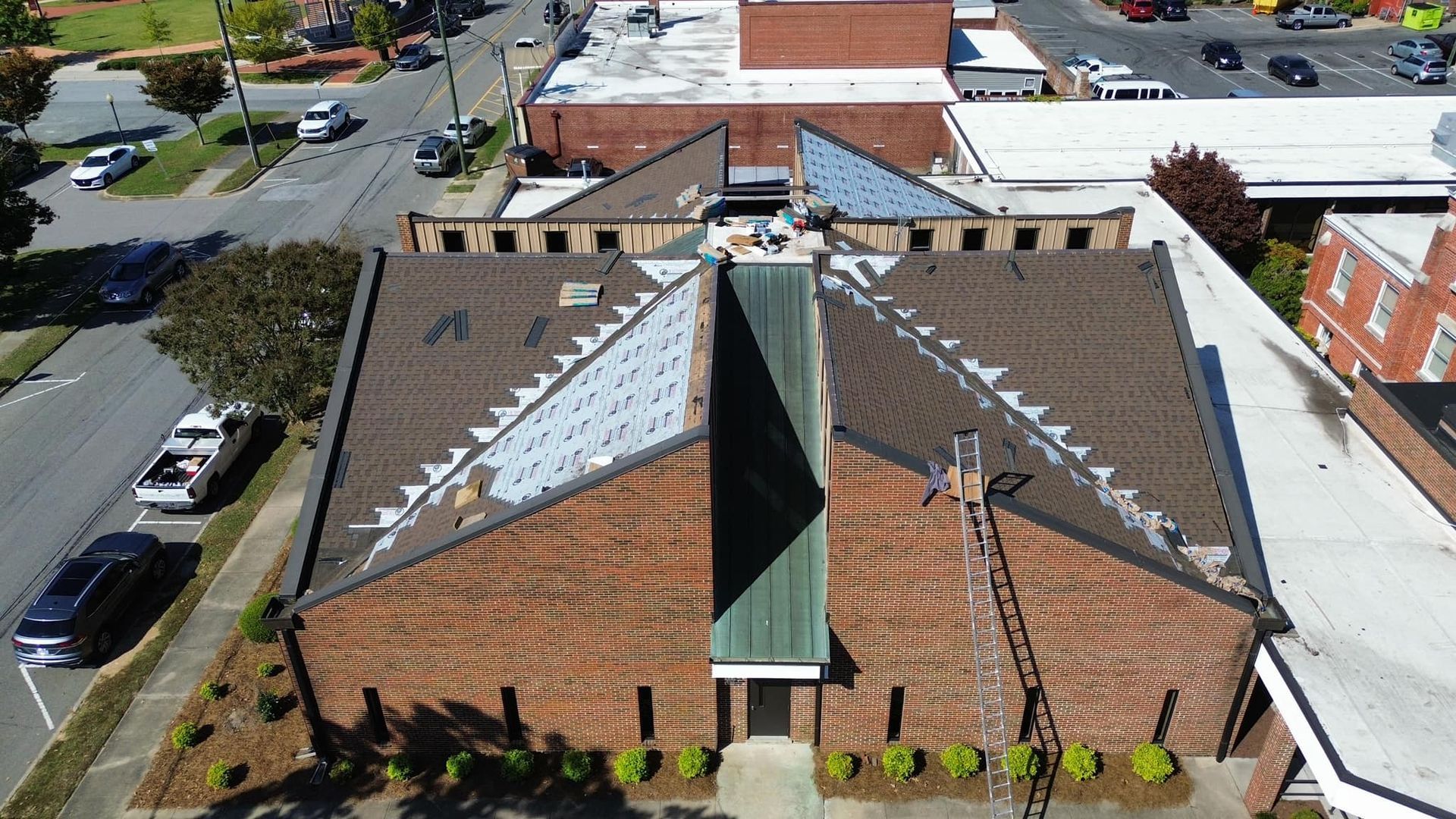 Aerial view of a brown brick building with a unique angled roof design; street with cars and trees in view.