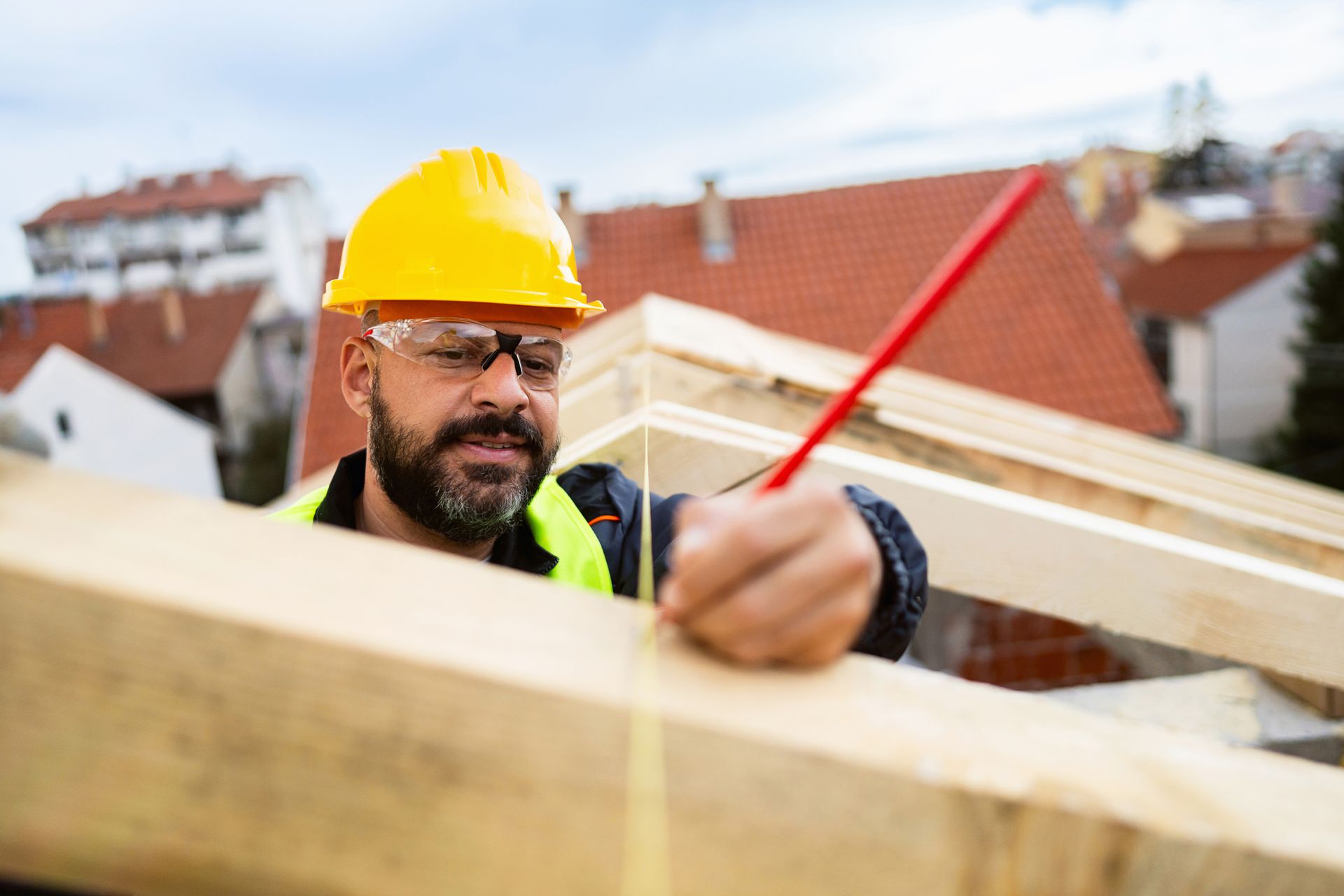 A roofer is measuring and marking the placement of timber while making a roof beam.