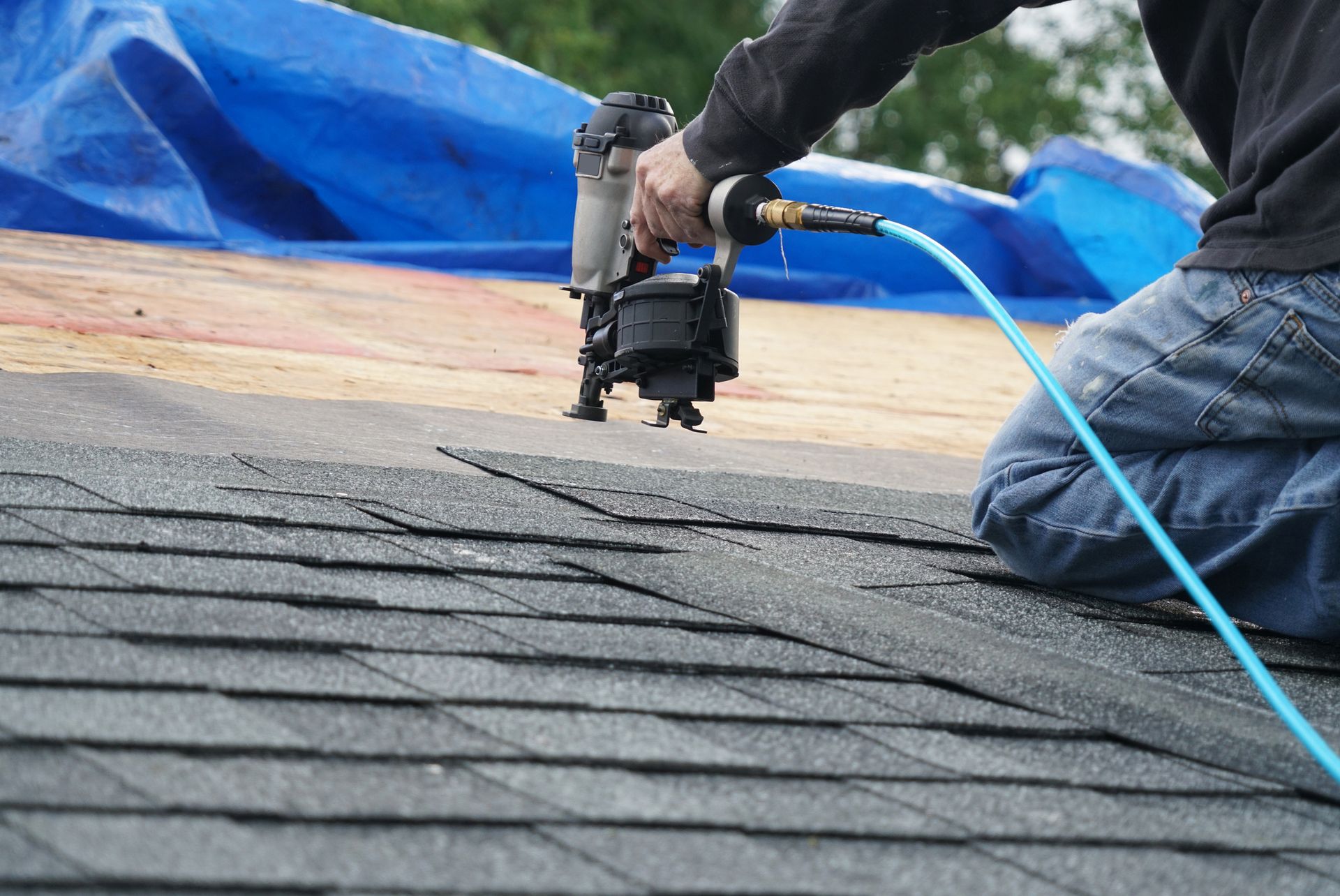 A roofing contractor using a nail gun to install shingles to repair the roof.