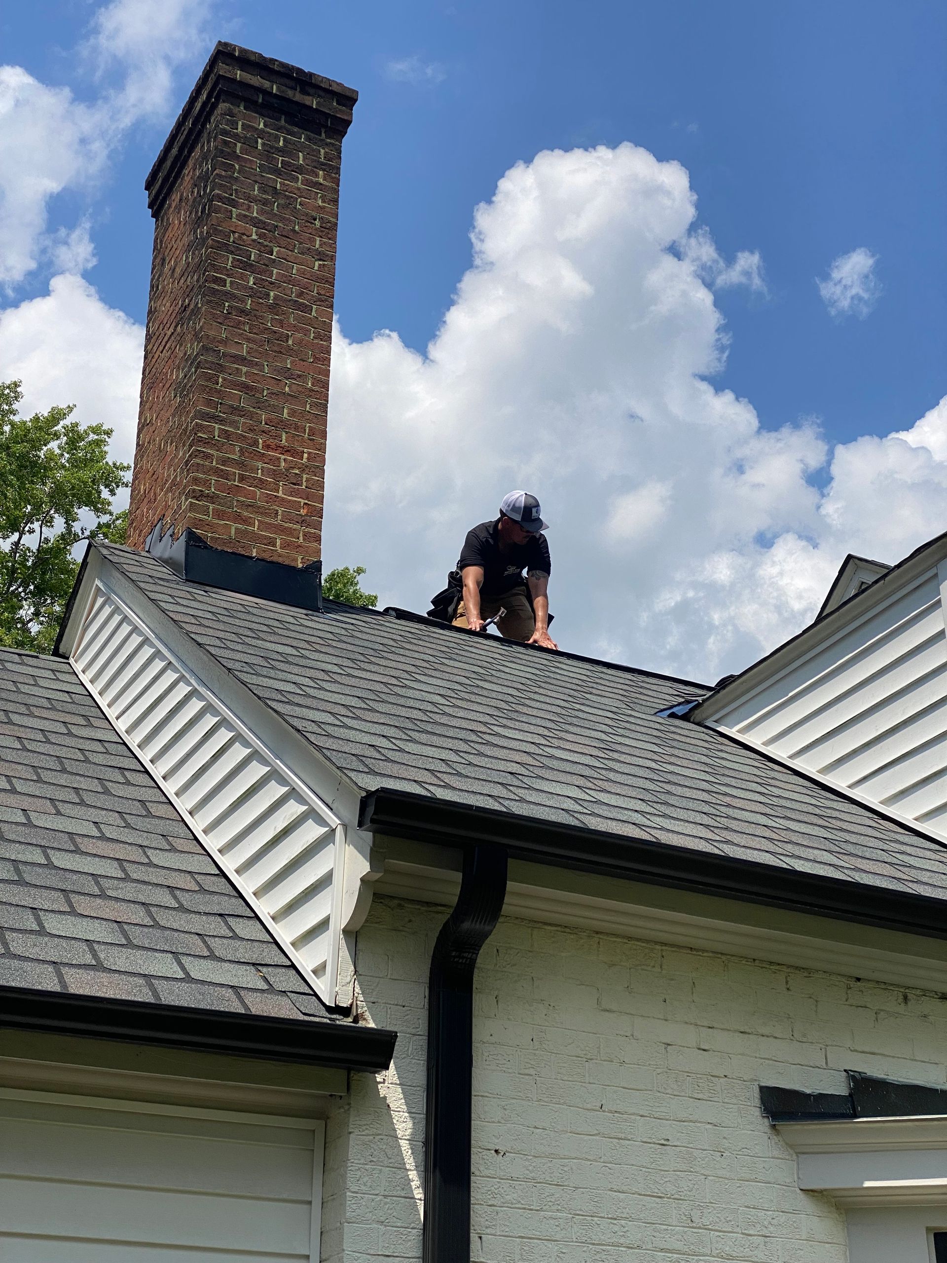 Person on a roof repairing a chimney; blue sky with clouds.