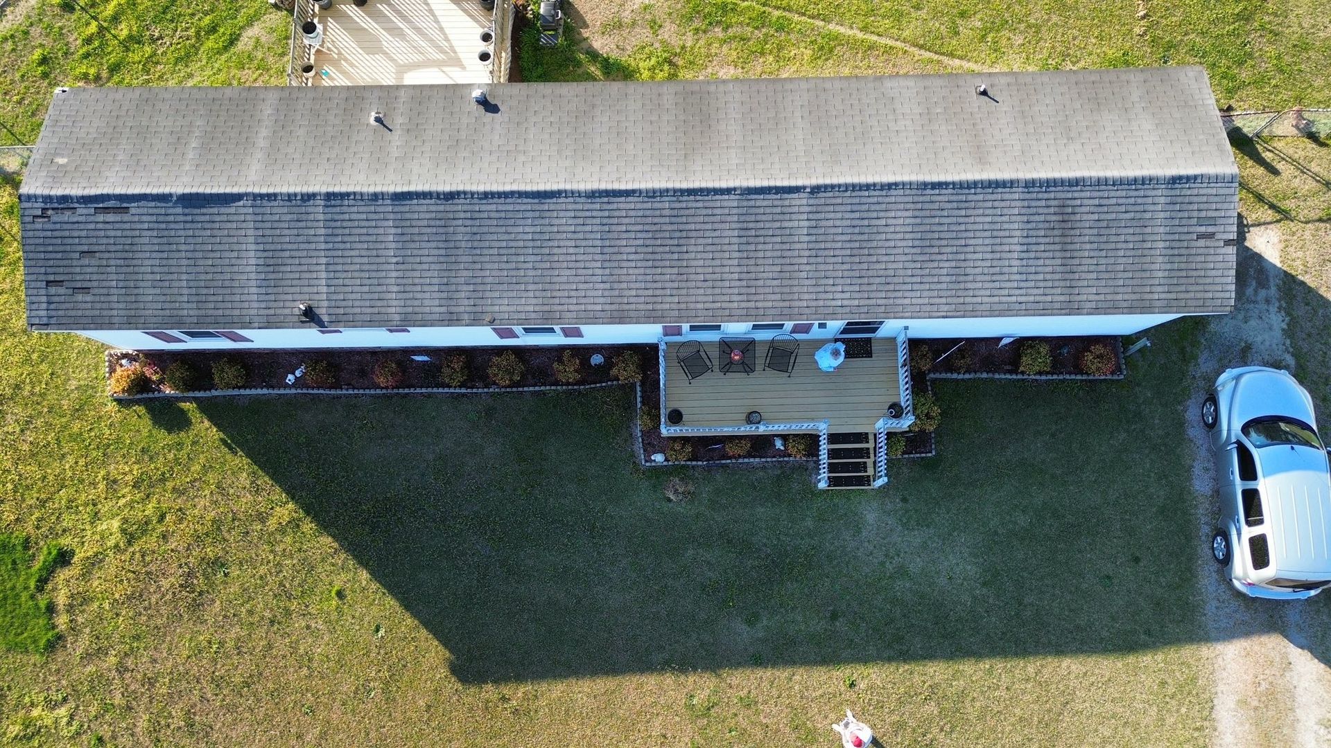 Overhead view of a house with a gray roof, small porch, and a white car in the driveway on a grassy yard.
