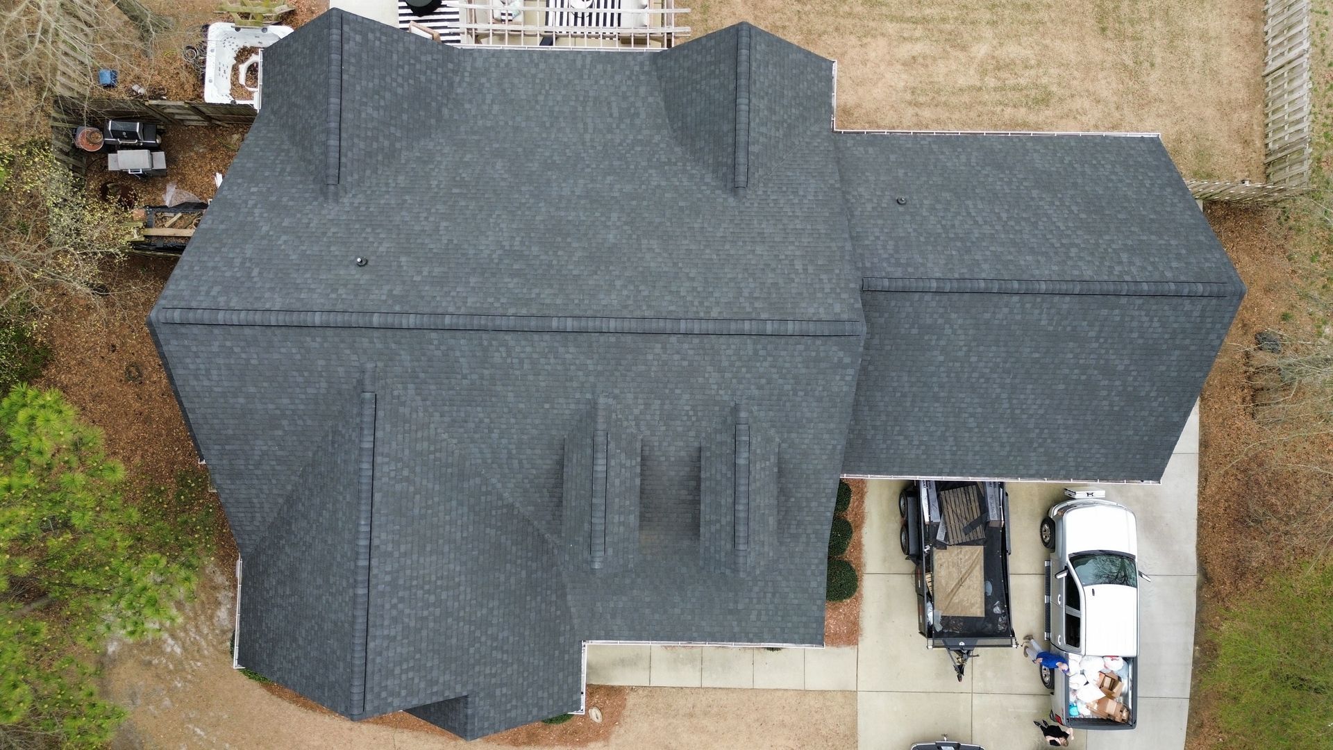 Overhead view of a house with a dark gray shingled roof, a truck, and a trailer in the driveway.