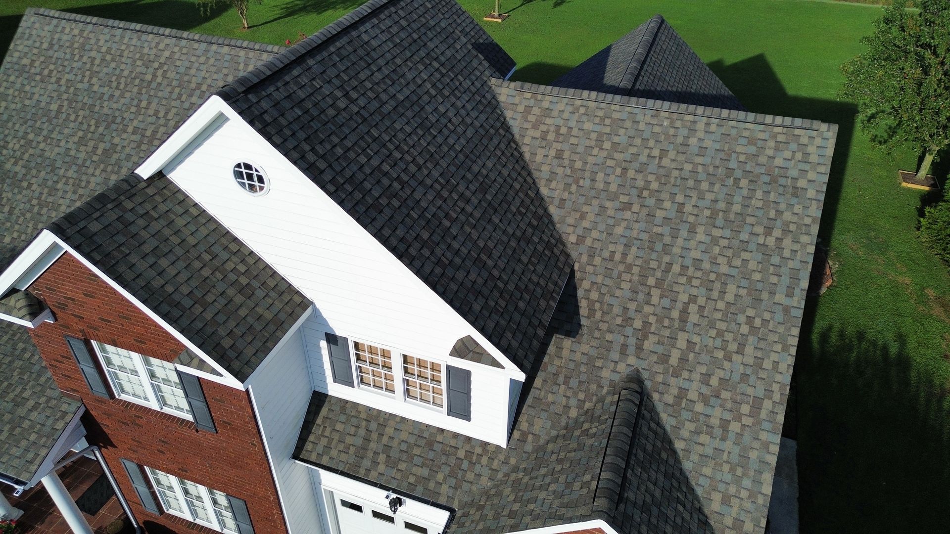 Overhead view of a house with a multi-gabled roof and brick and white siding. Green grass surrounds.