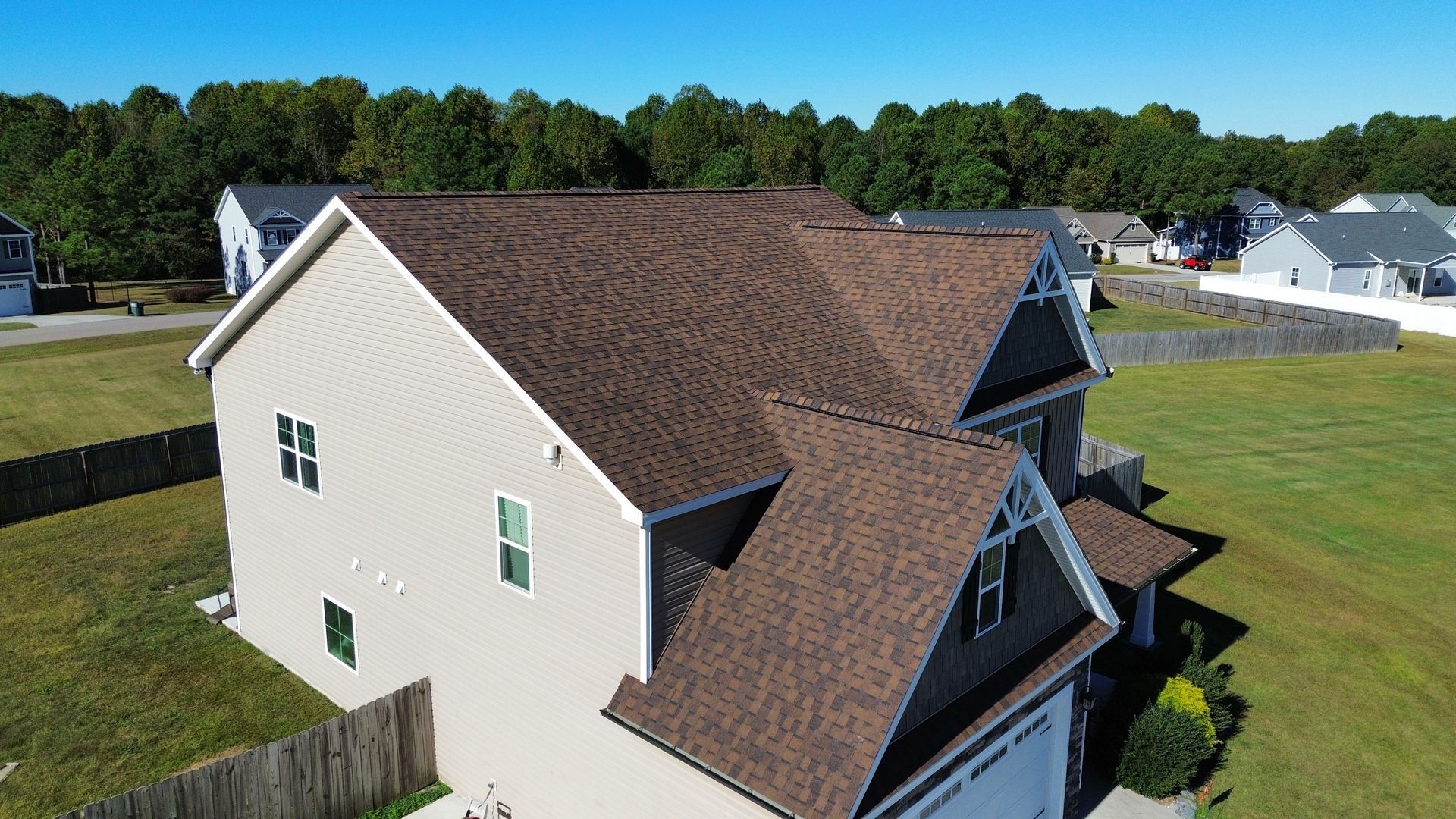 House with brown roof and beige siding, in a grassy yard, with a clear blue sky.