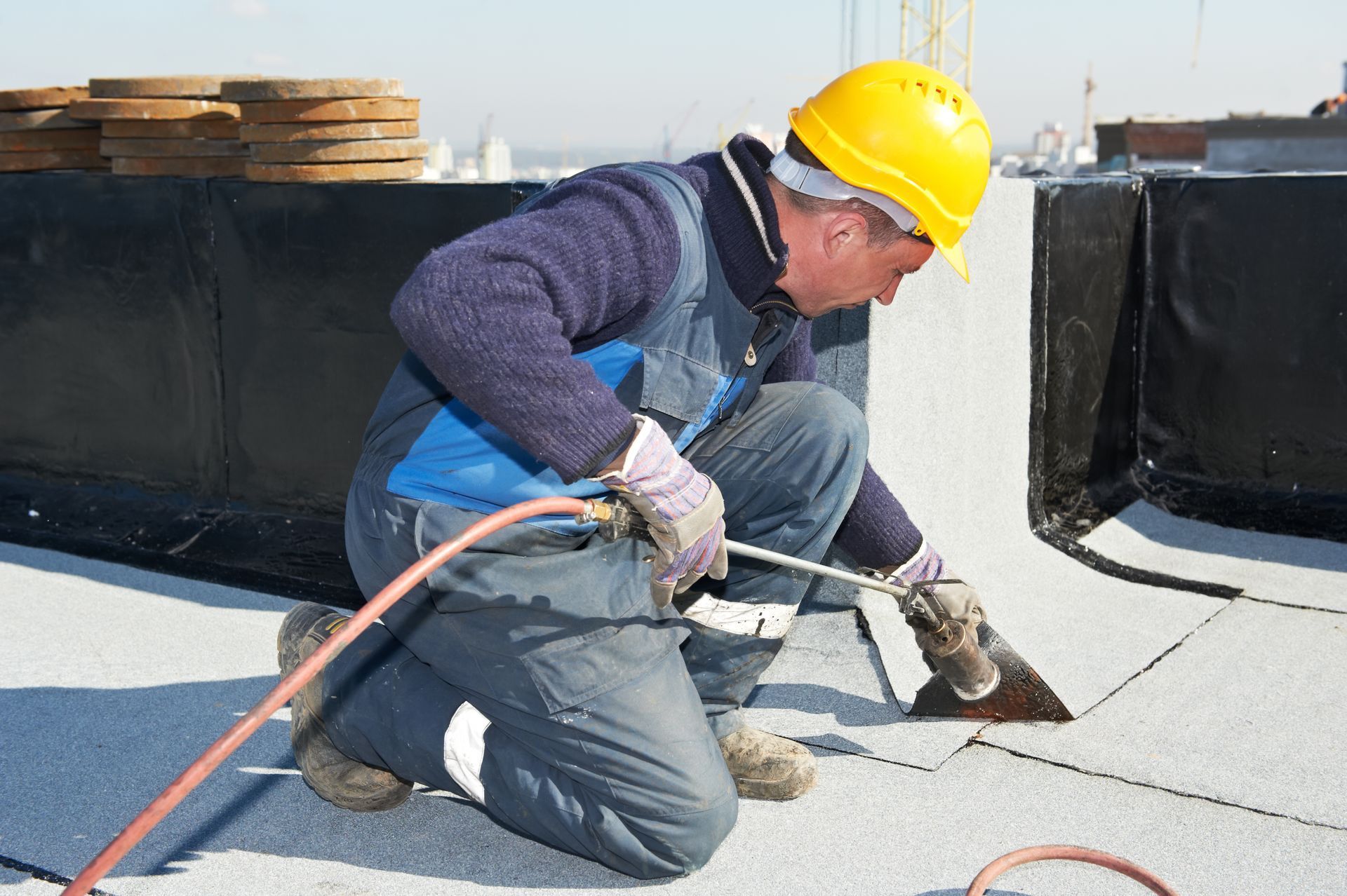 A roofer is installing roofing felt with a heating and melting roll by torch on flame.
