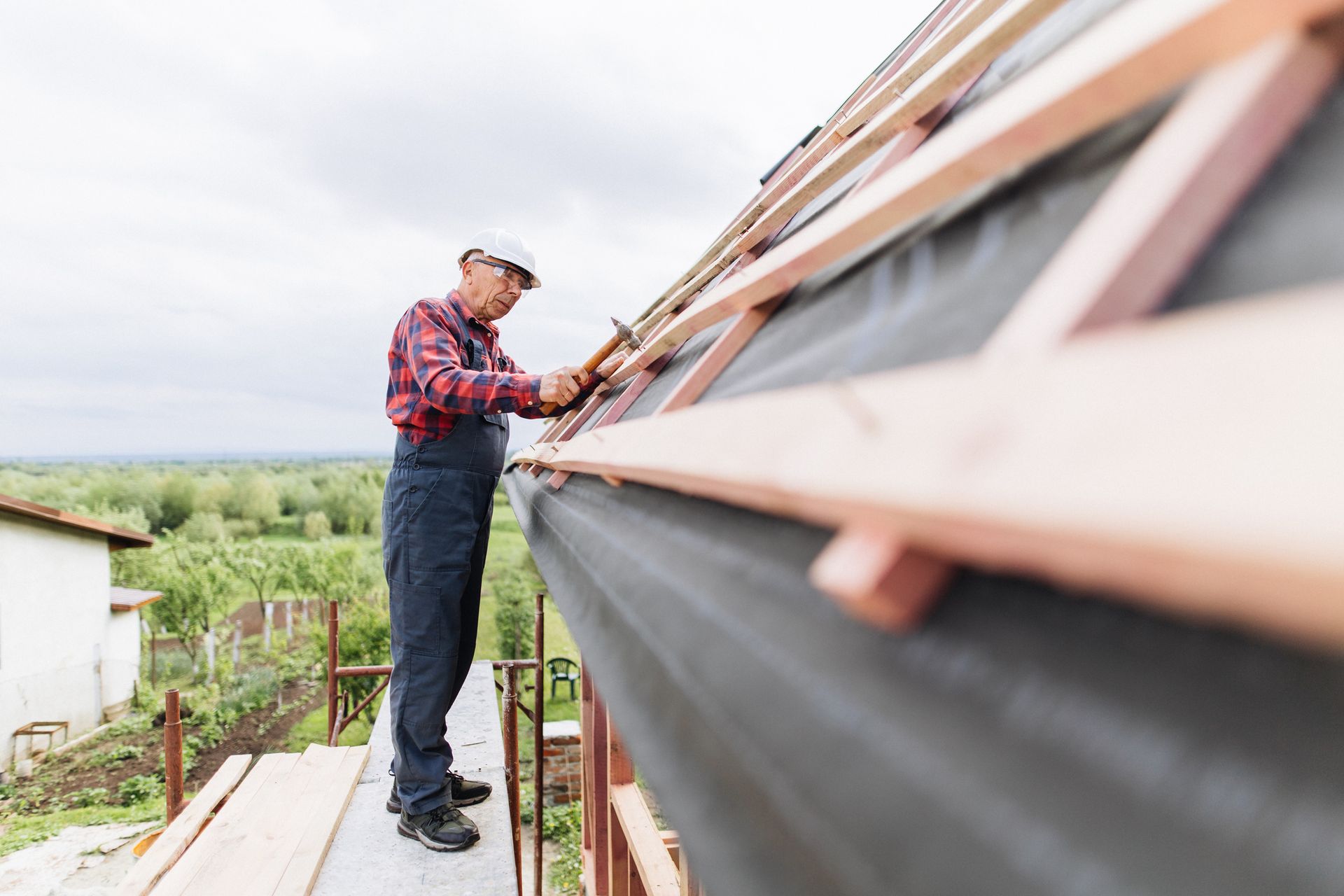 Roofer installing wooden battens on sloped roof frame while working outdoors on residential project.