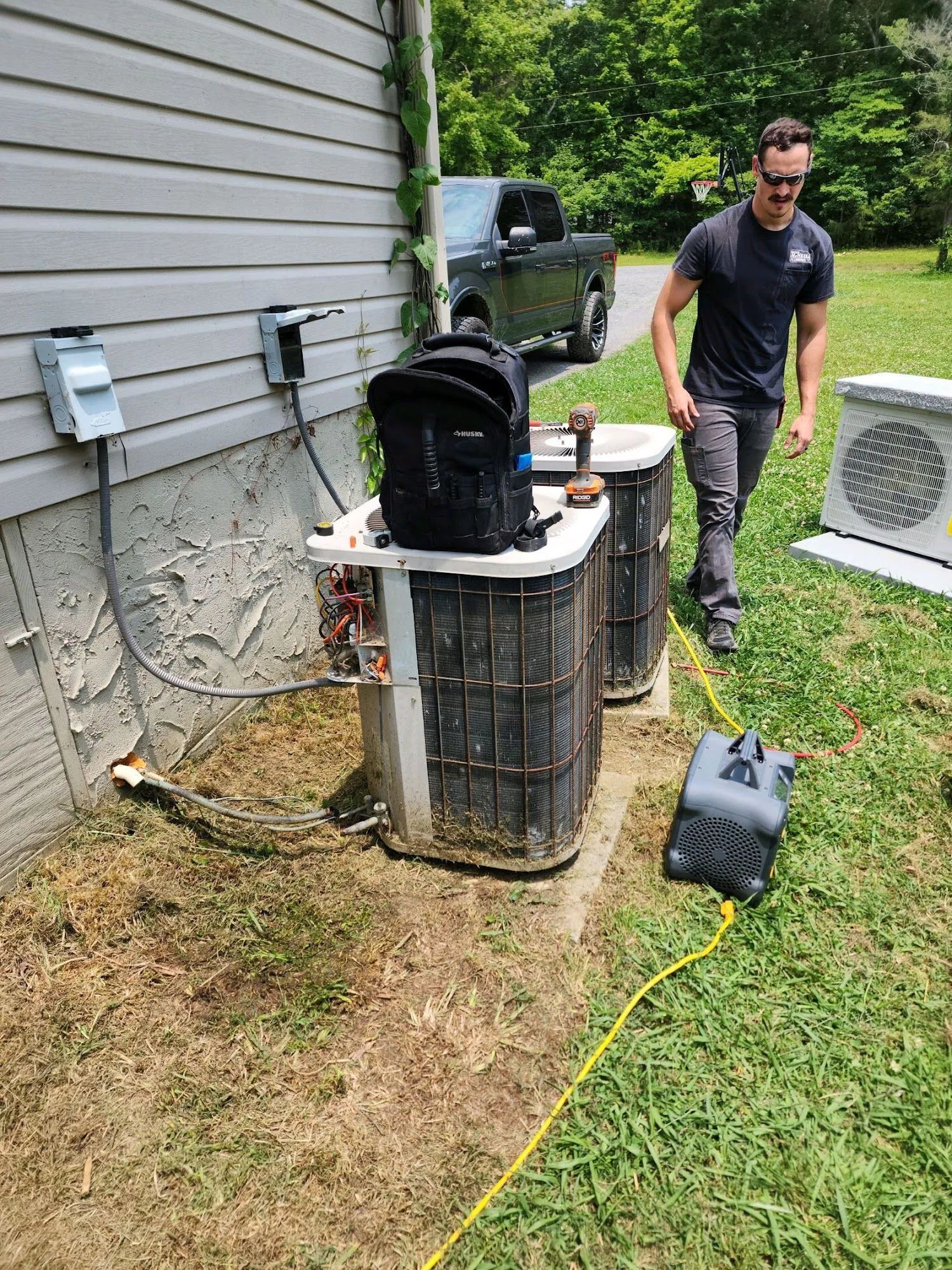 HVAC technician working on two outdoor air conditioning units near a house.