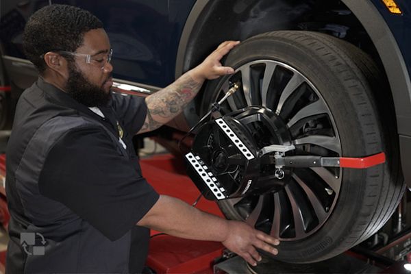 Mechanic adjusting a wheel alignment device on a car tire in a garage, wearing safety glasses.