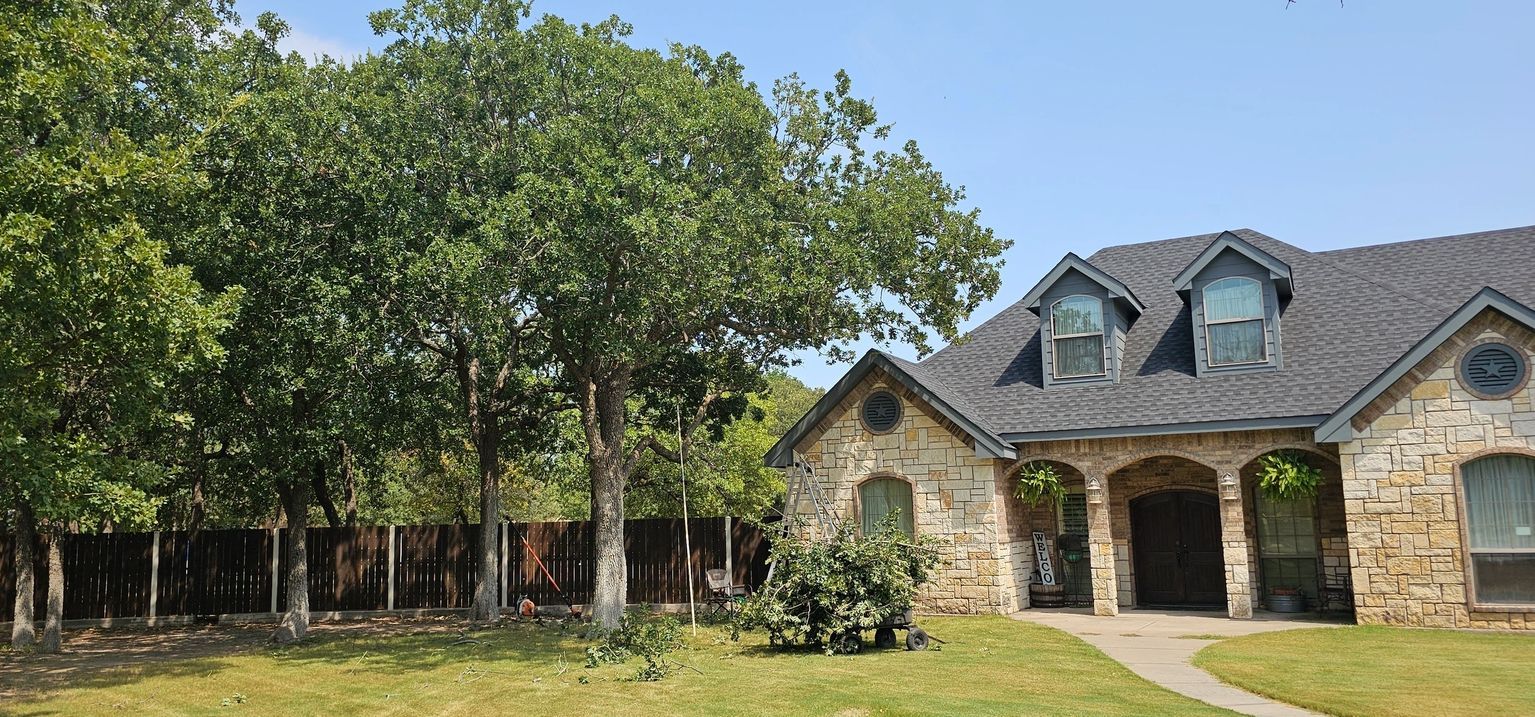 A large stone house with a gray roof is surrounded by trees.
