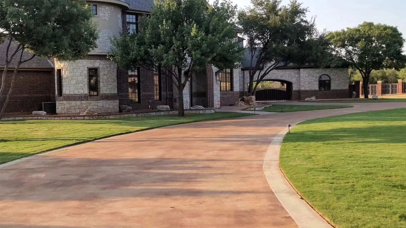 A driveway leading to a large house surrounded by trees and grass.