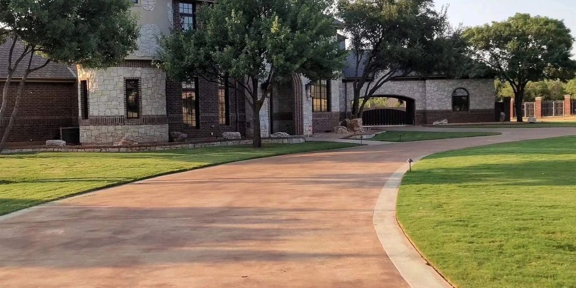 A driveway leading to a large house surrounded by trees and grass.
