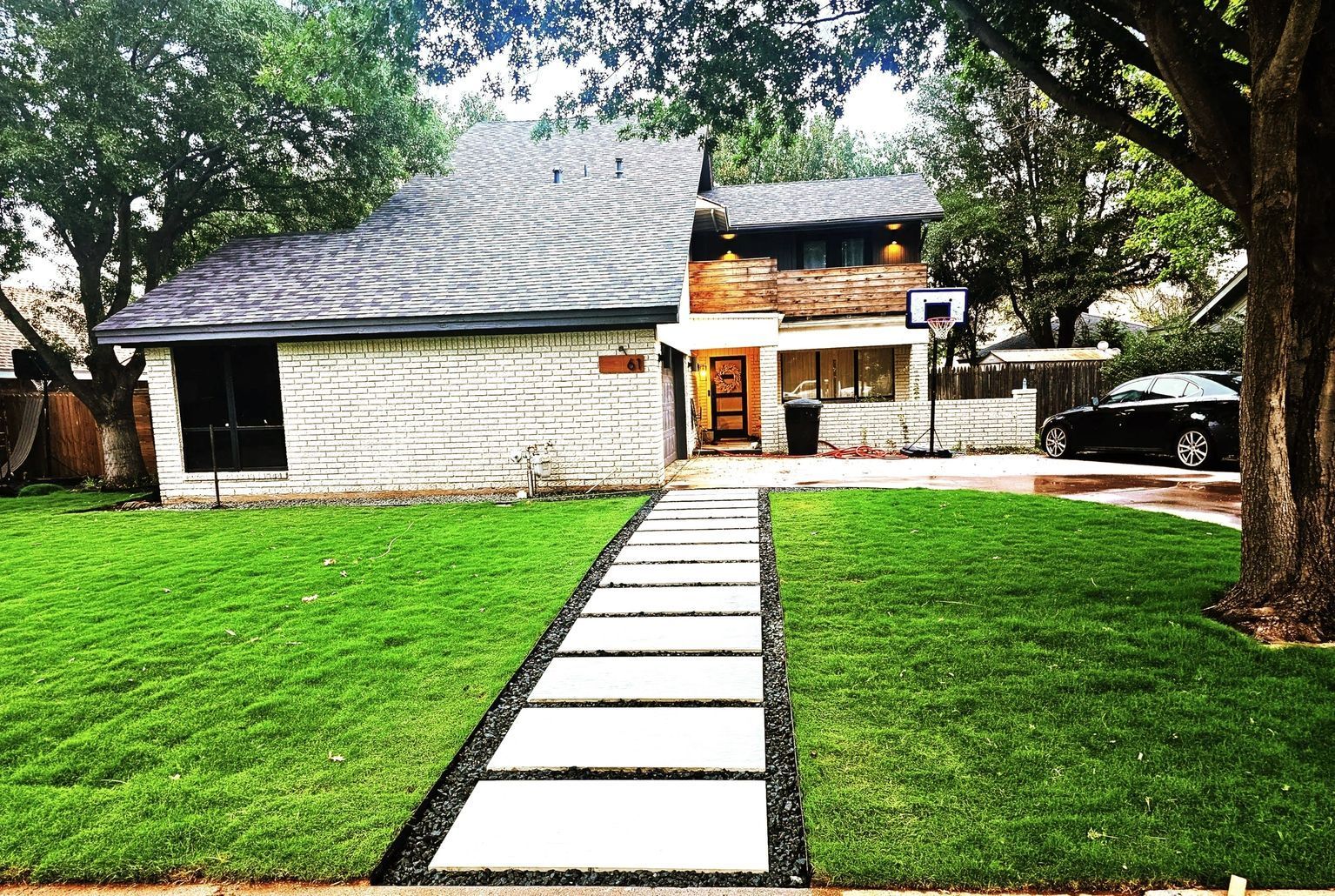A house with a basketball hoop in the backyard and a walkway leading to it.
