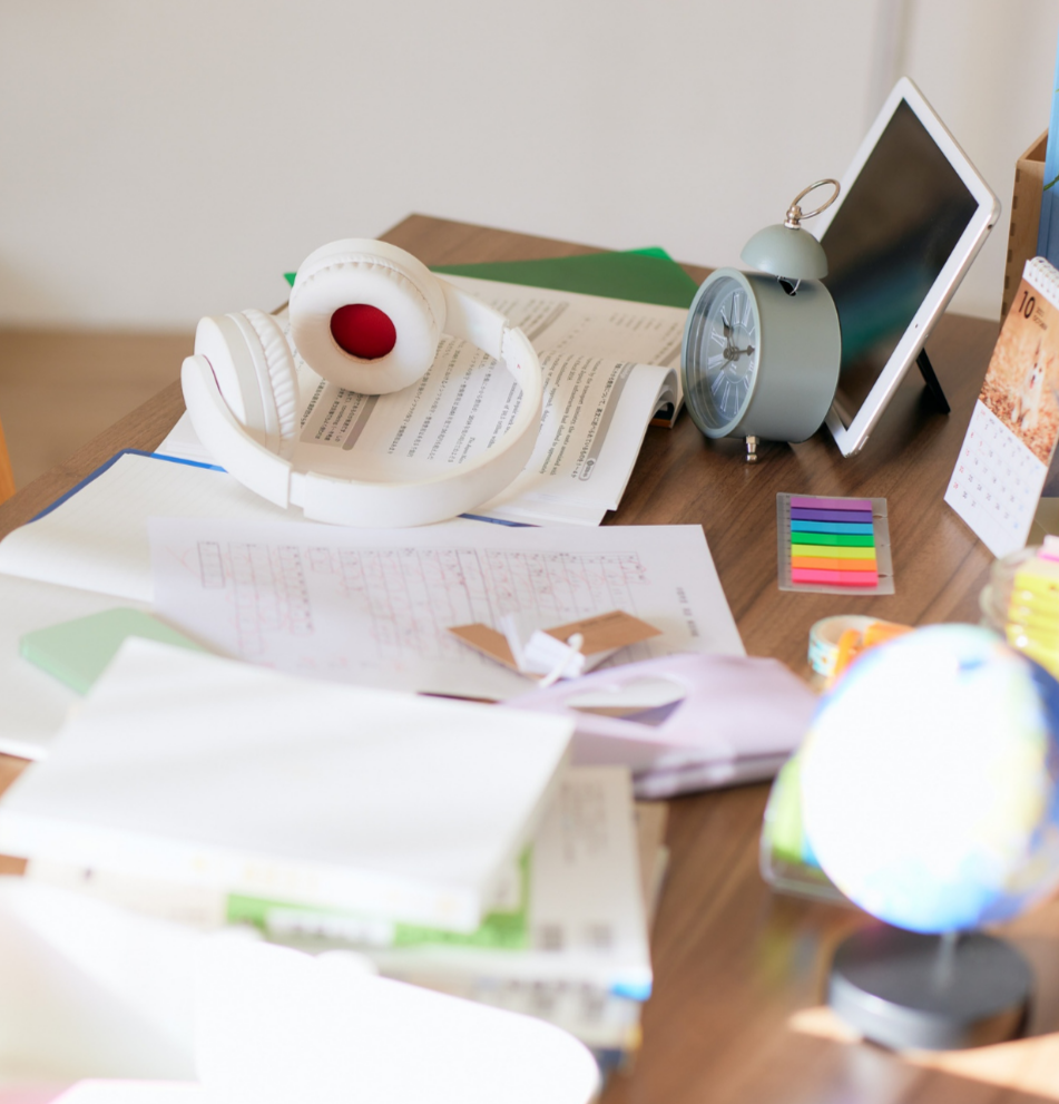 Desk with papers, headphones, tablet, and alarm clock.