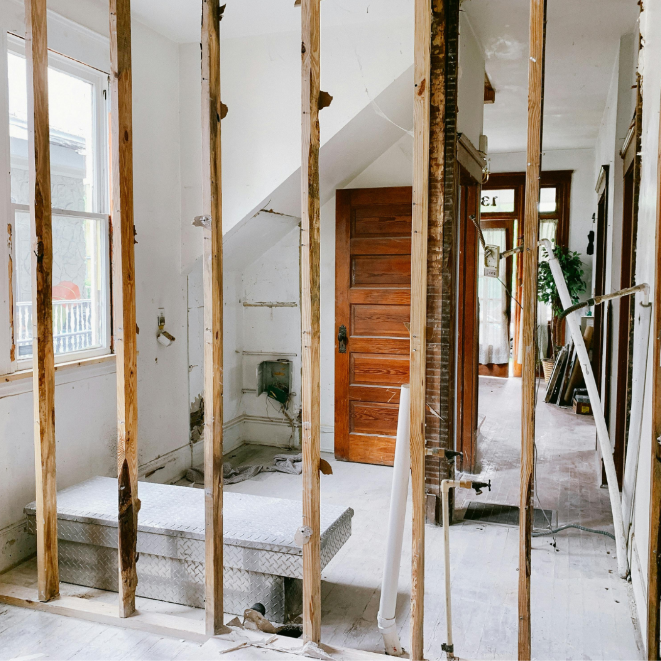 Bathroom renovation with exposed studs, old door, and hallway in a house.