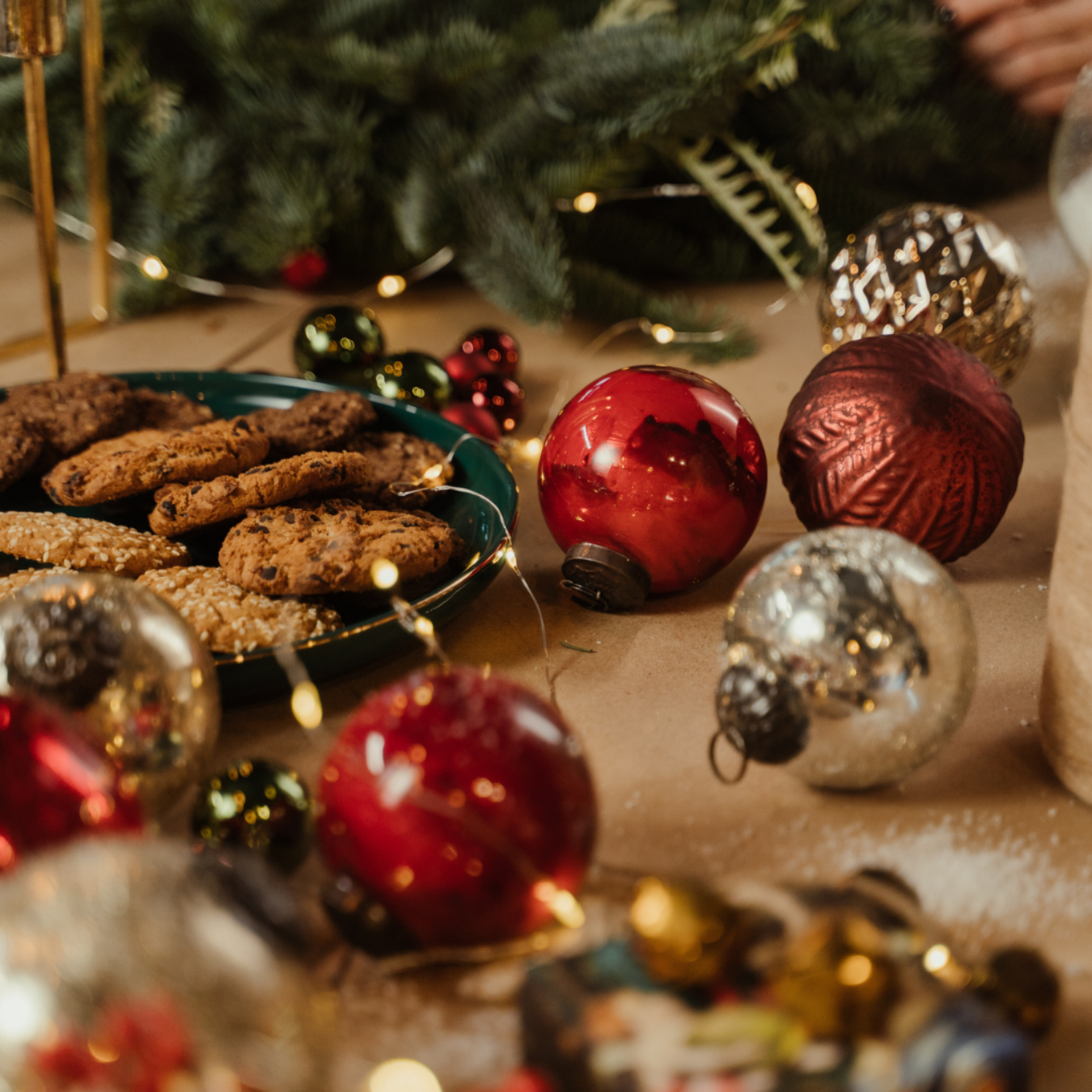 Christmas scene: cookies on a plate, red and silver ornaments, and fairy lights on a wooden surface.
