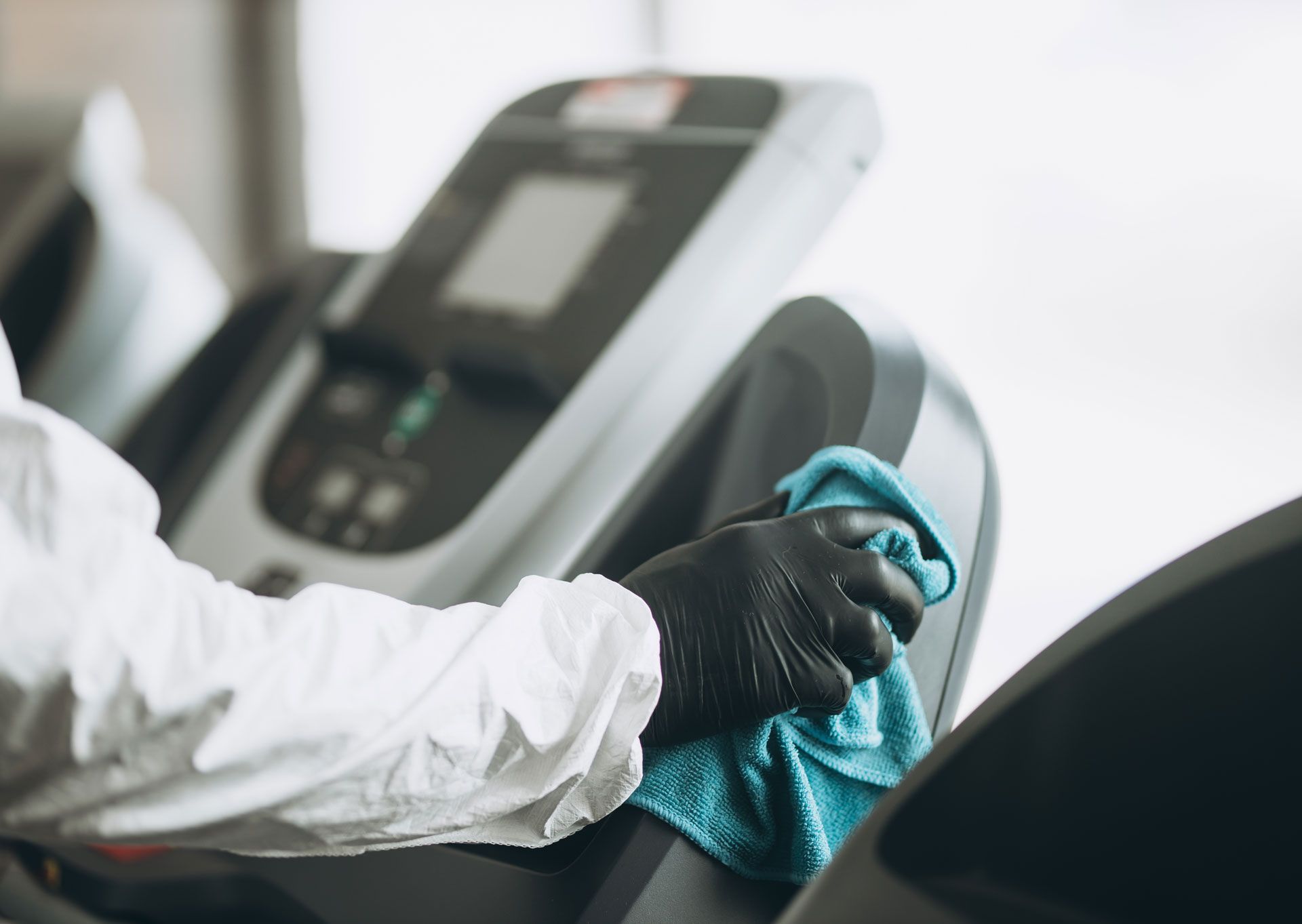 Person in protective suit cleaning treadmill with blue cloth.
