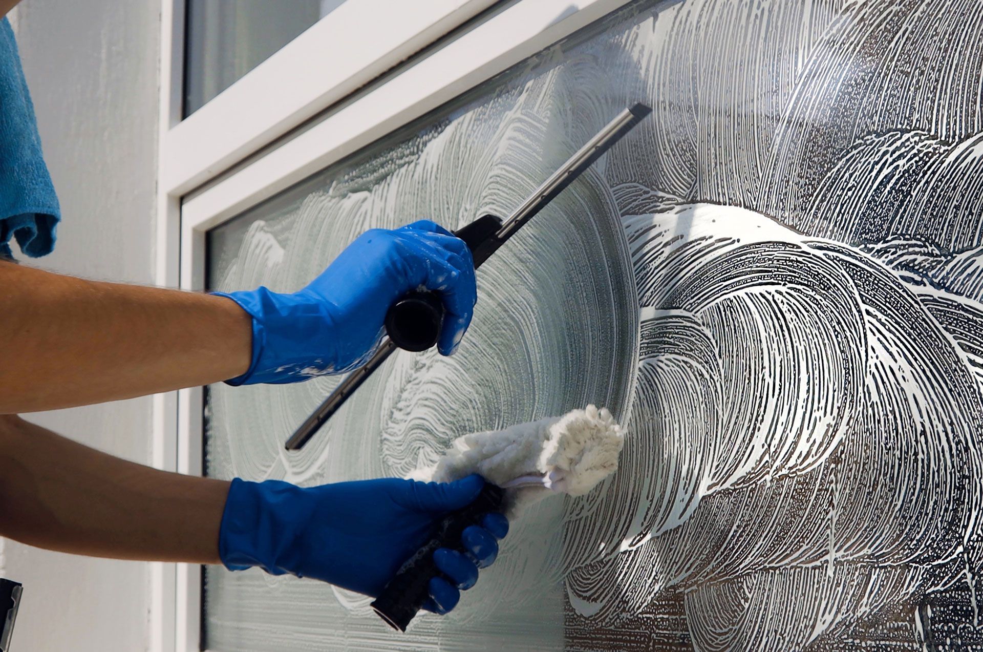 Person washing a window with a squeegee and soapy water, wearing blue gloves.