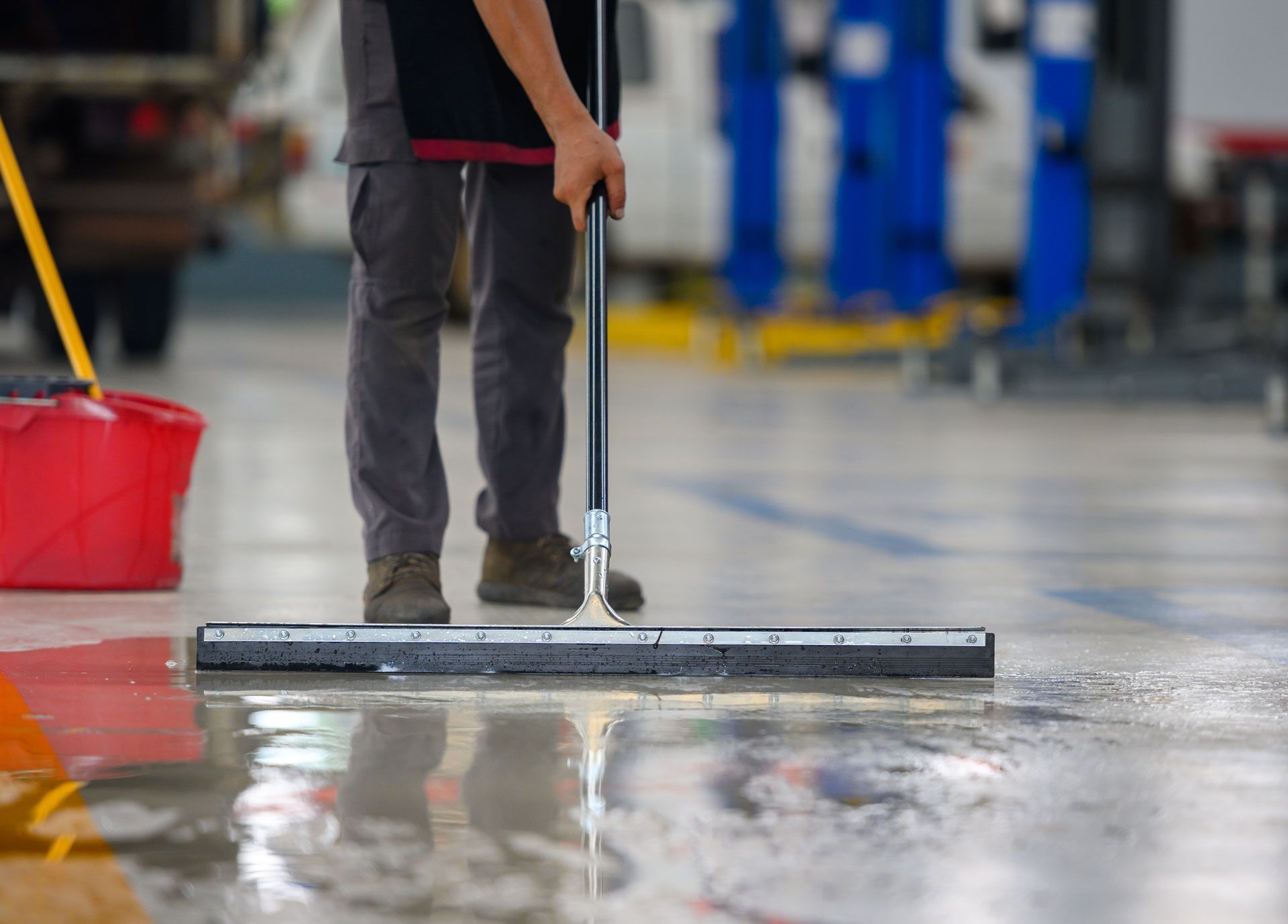 Person mopping a wet concrete floor in an industrial setting, using a squeegee.