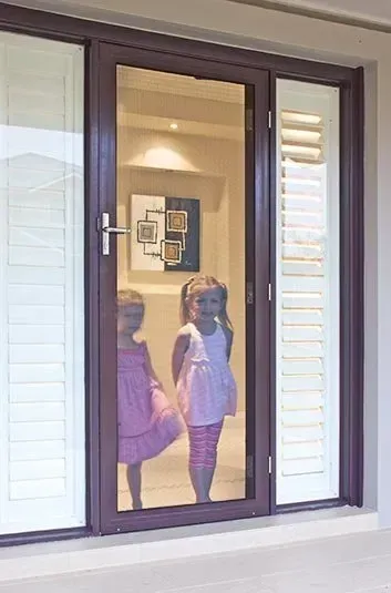 Two Young Girls Looking Through a Glass Door — Big Tom's Security Screens in Farleigh, QLD