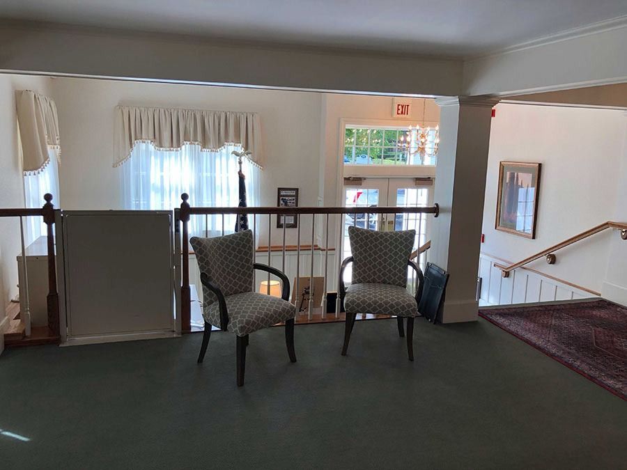 Two patterned chairs on a second-floor landing with railings, doorway, and windows.