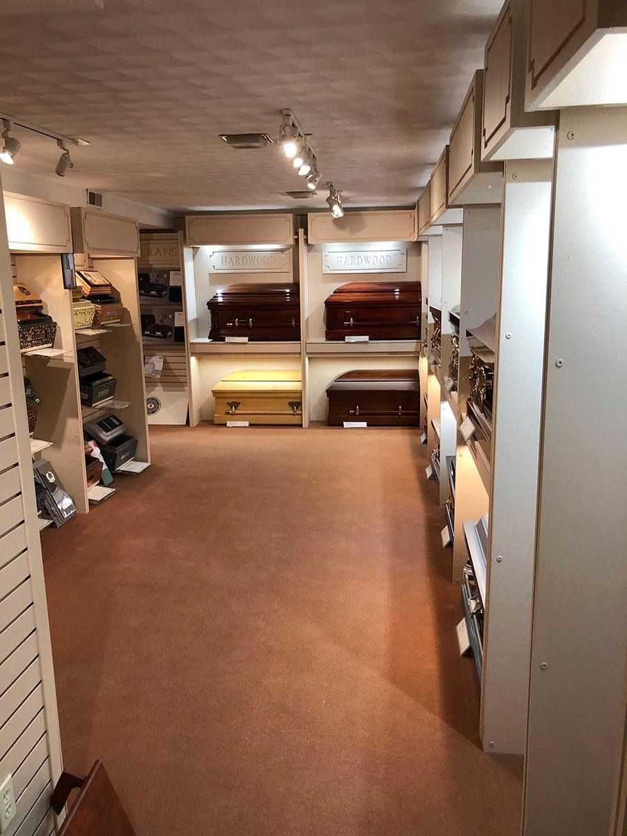 Interior of a funeral home displaying several coffins in a carpeted room with overhead lighting.