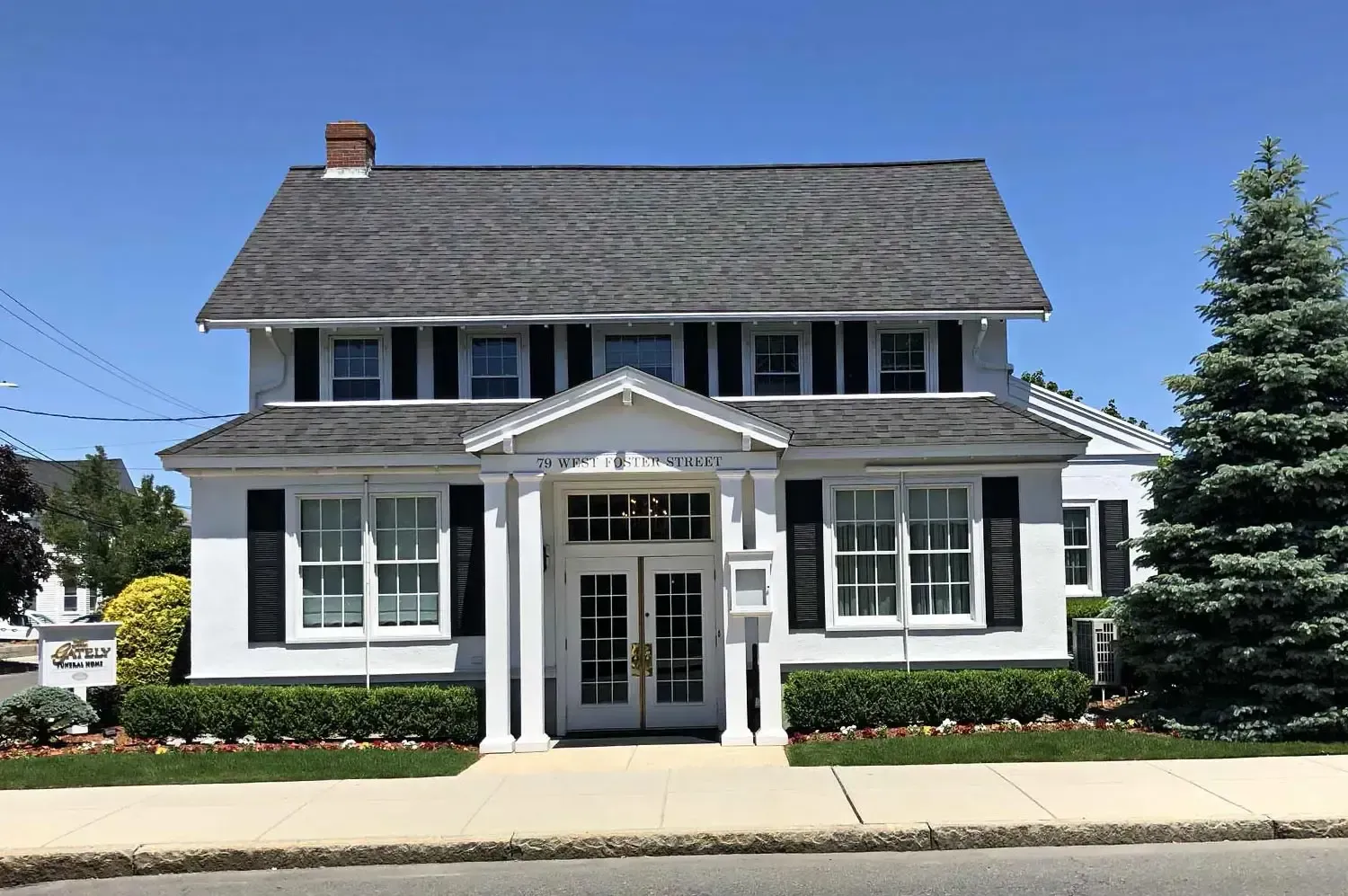 White two-story building with black shutters and a small porch. A tree is on the right side.