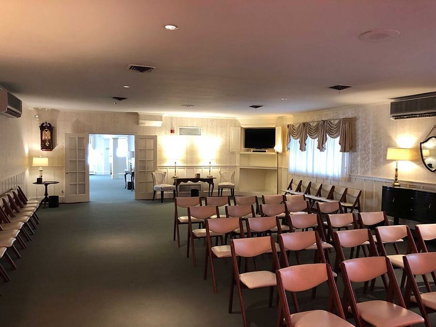 Funeral home viewing room, rows of pink chairs face a fireplace and a TV.