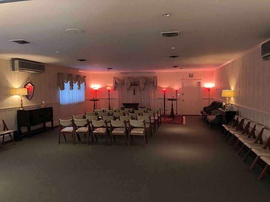 Funeral home interior with chairs arranged for a service, red lighting, and a dark wooden altar.