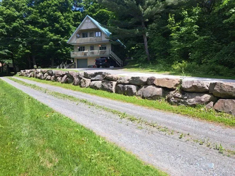 Un chemin de terre menant à une maison entourée d'arbres et de rochers.
