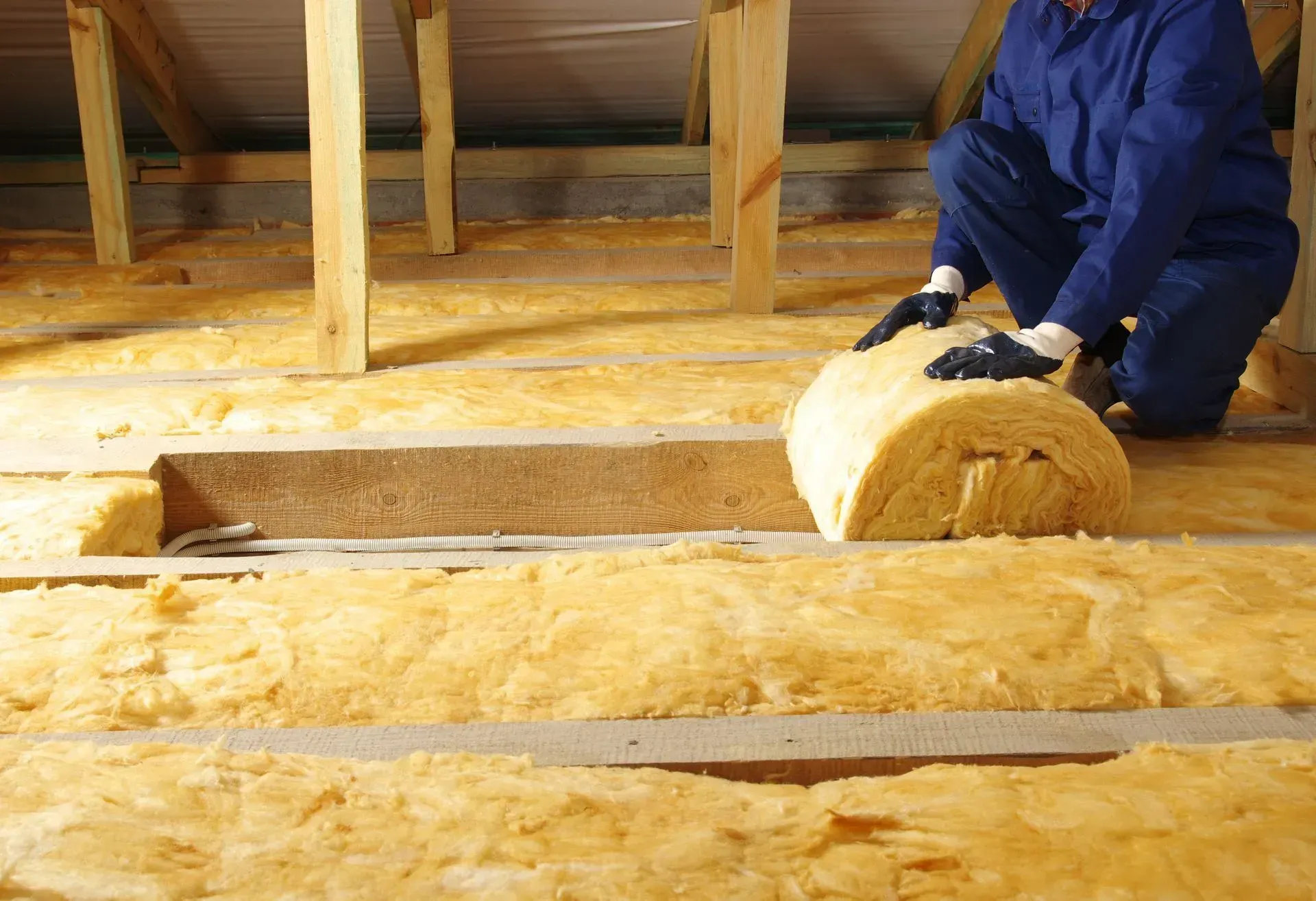 Un homme pose de l'isolant sur le sol d'un grenier.